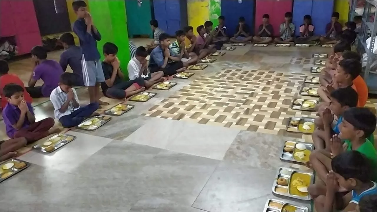 Children sitting together on the floor with meal trays.