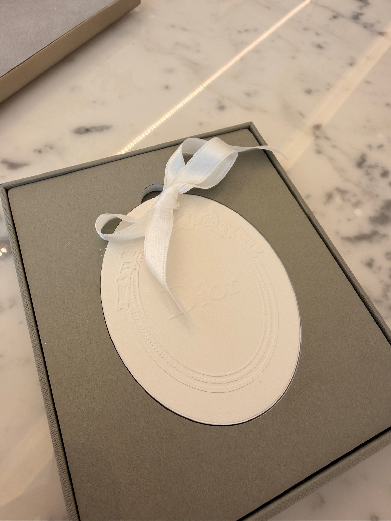 A gray gift box with a white ribbon bow on a marble countertop.