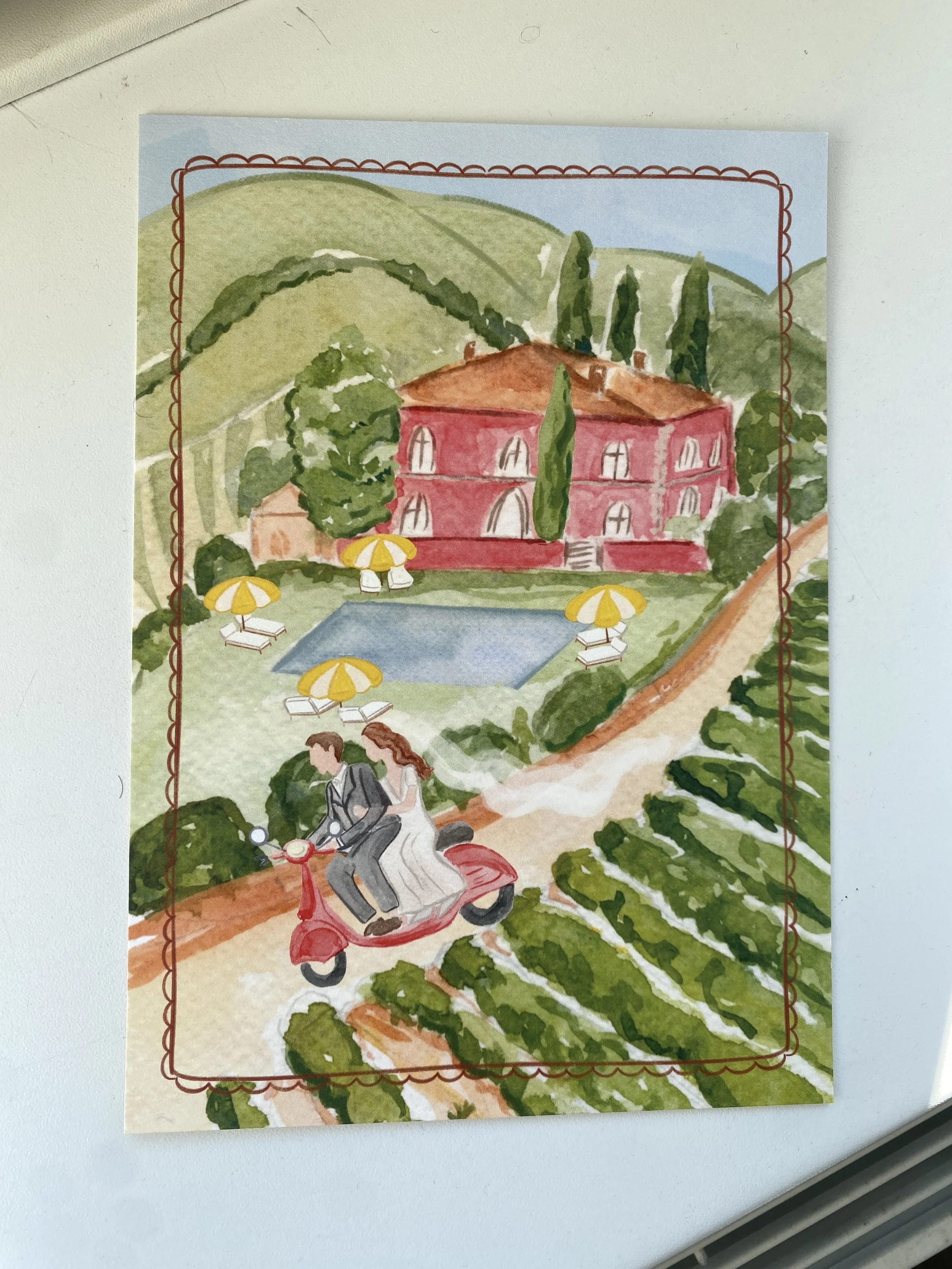 Colorful watercolor illustration of a hillside estate with a red building, surrounded by green trees and hills, with a swimming pool and lounging chairs with yellow umbrellas in the foreground.