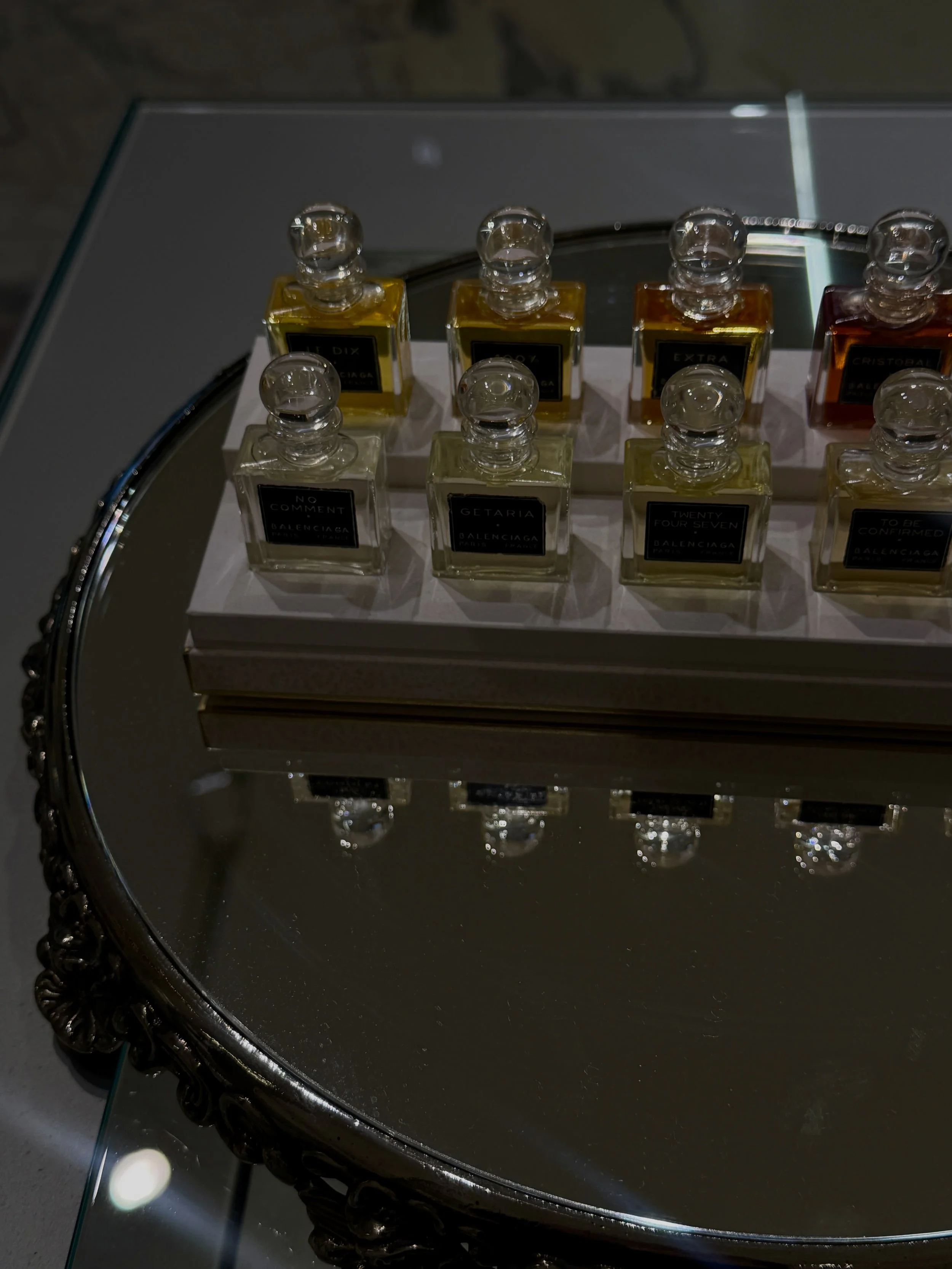 Set of Balenciaga perfumes in rectangular bottles with black labels, placed on a mirrored surface on a silver tray with decorative edge.