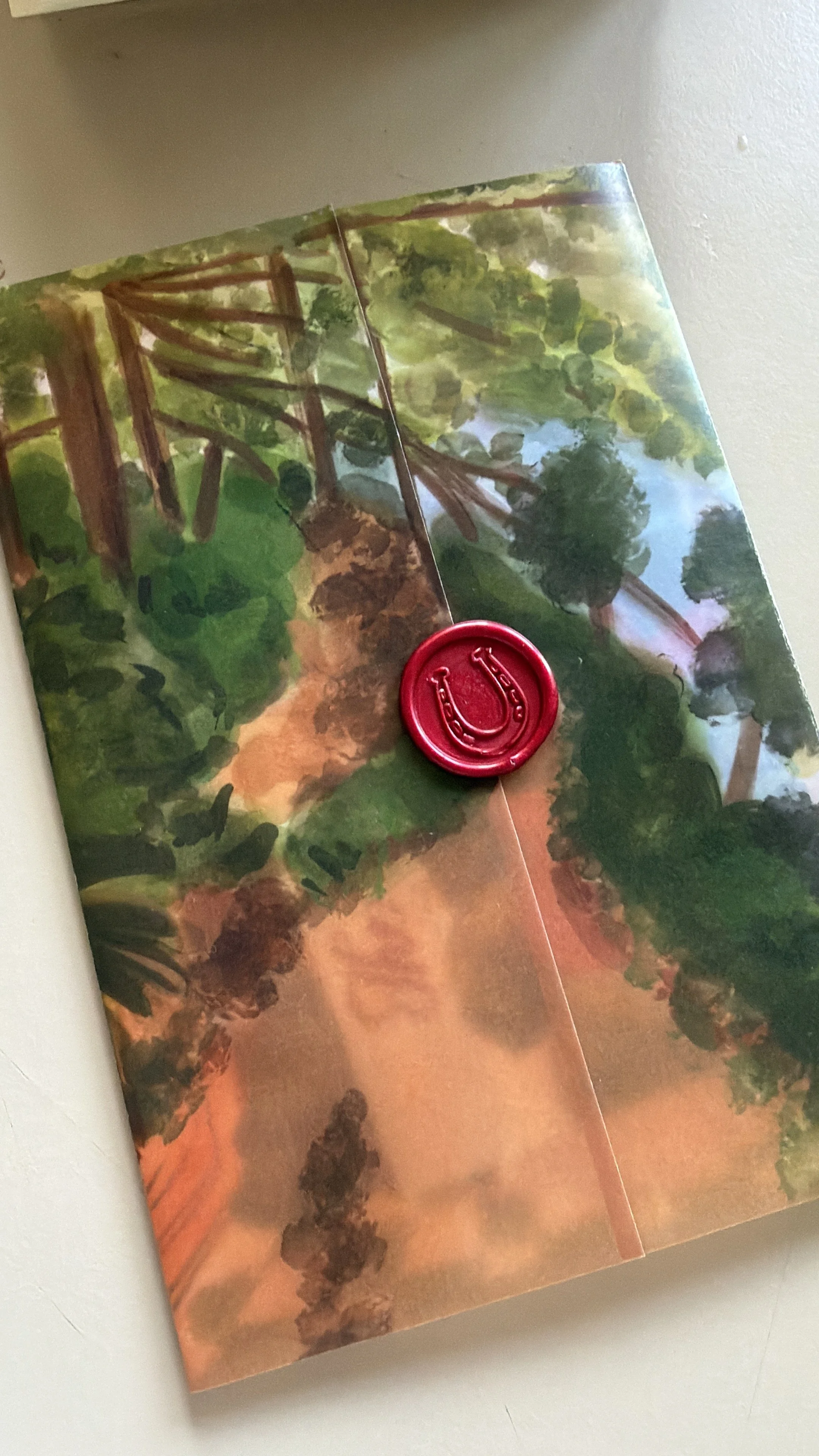 A booklet with a landscape painting of trees and a trail, sealed with a red wax stamp.