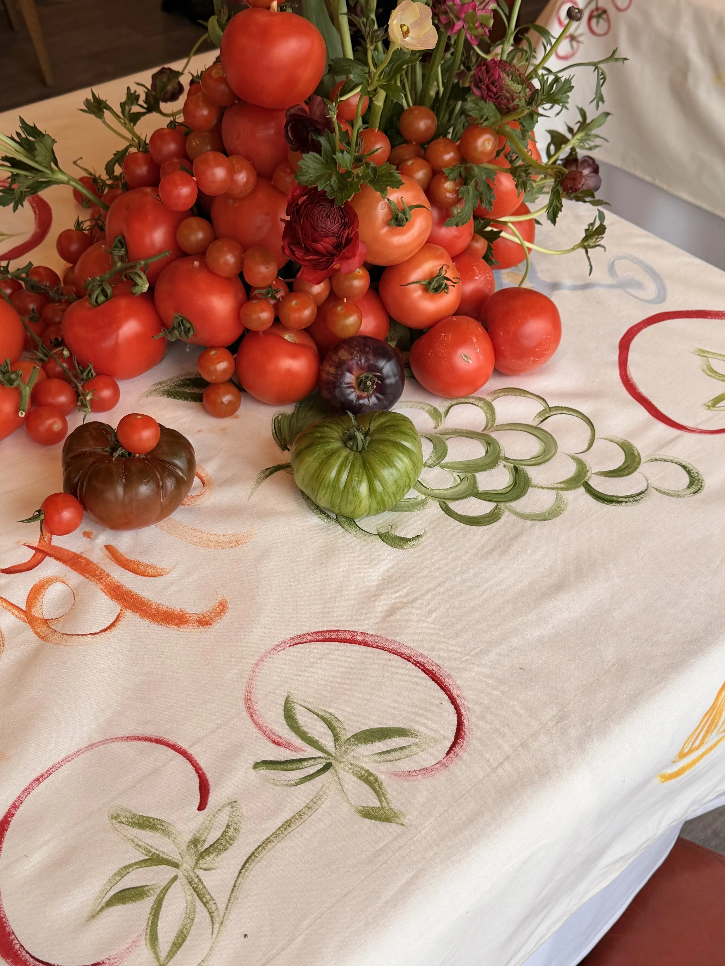 A floral arrangement of tomatoes and flowers on a table with a decorative tablecloth.