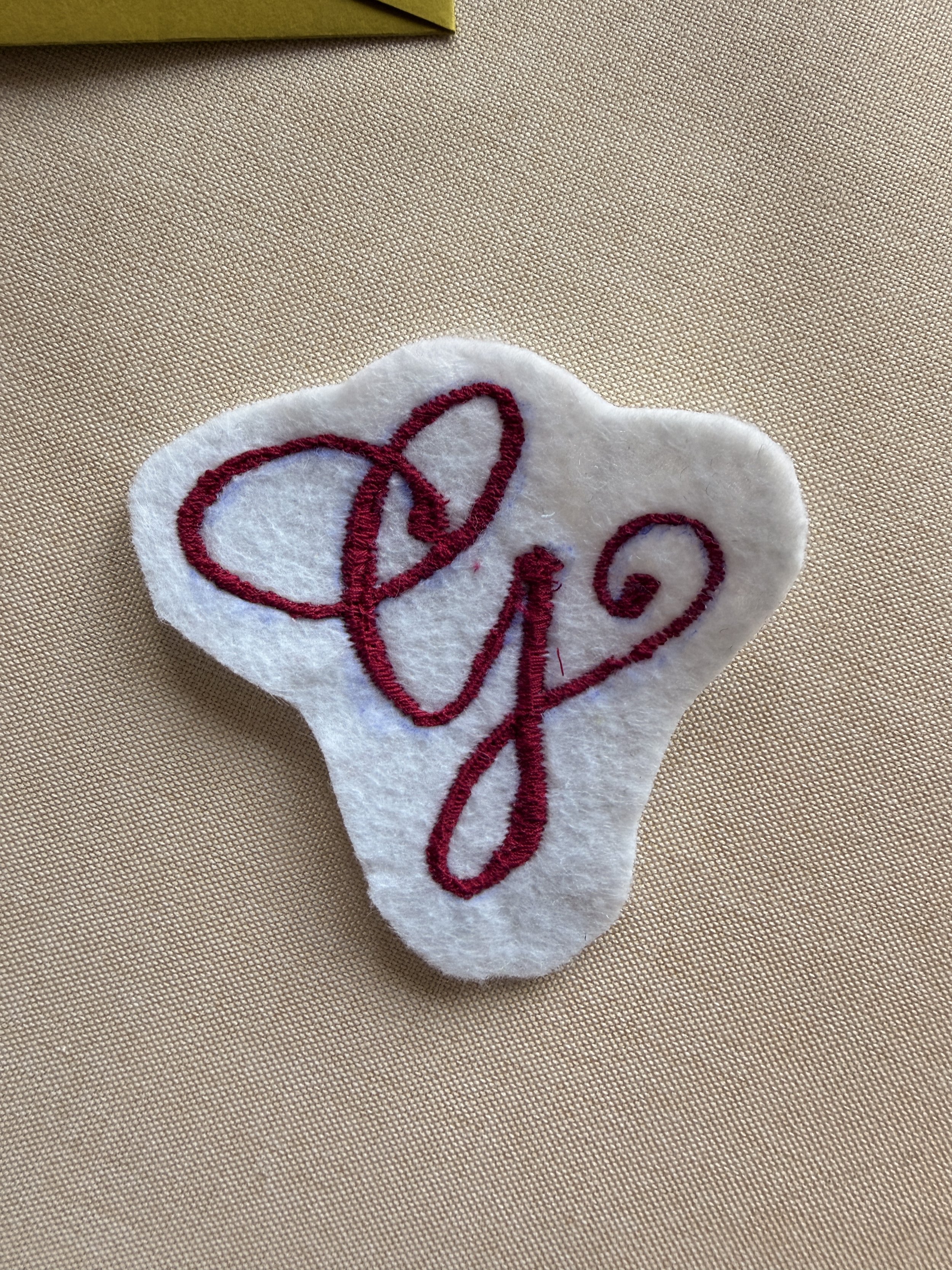 Close-up of a white fabric with red embroidered cursive text, lying on a beige textured surface.