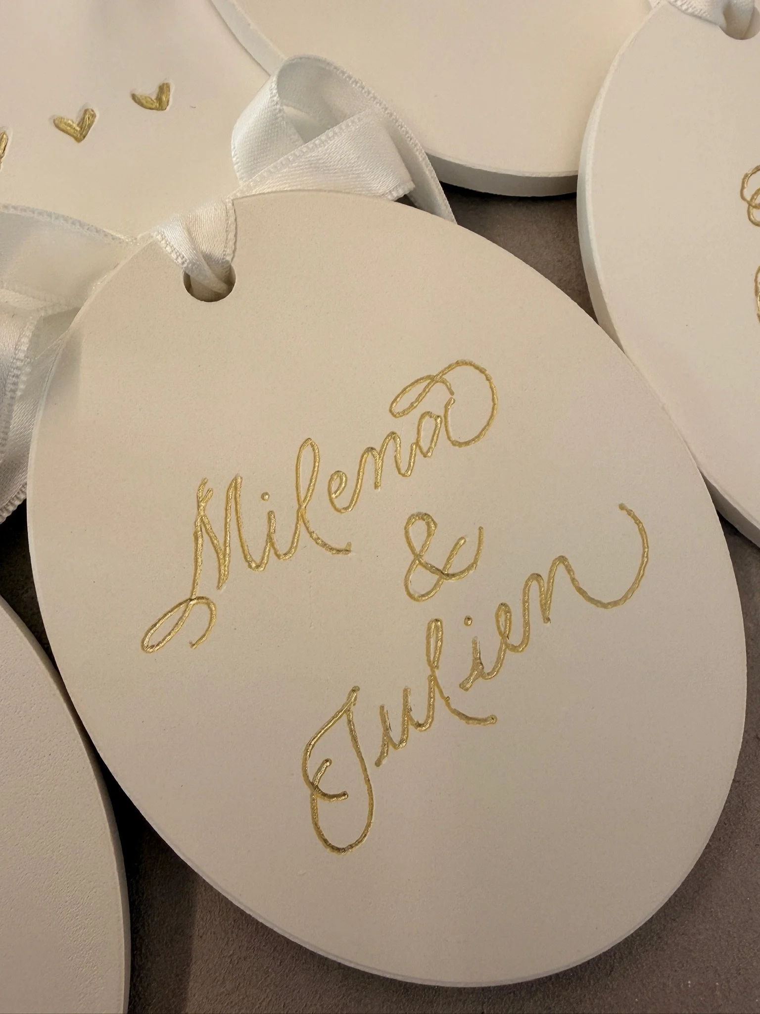 Close-up of a white heart-shaped card with gold cursive writing and a white ribbon.