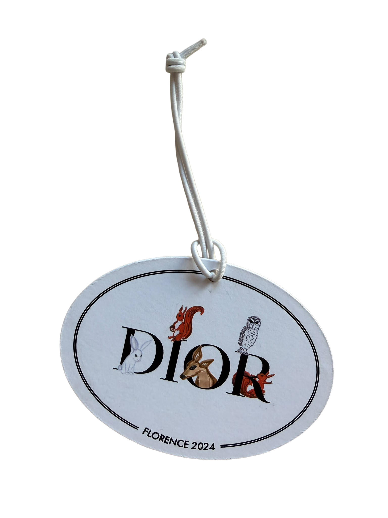 A circular souvenir badge with the word 'Dior' in large black font, featuring illustrations of various animals including a rabbit, a squirrel, an owl, a deer, and a fox, with the text 'FLORENCE 2024' at the bottom. The badge is hanging from a white string attached to a silver hook.