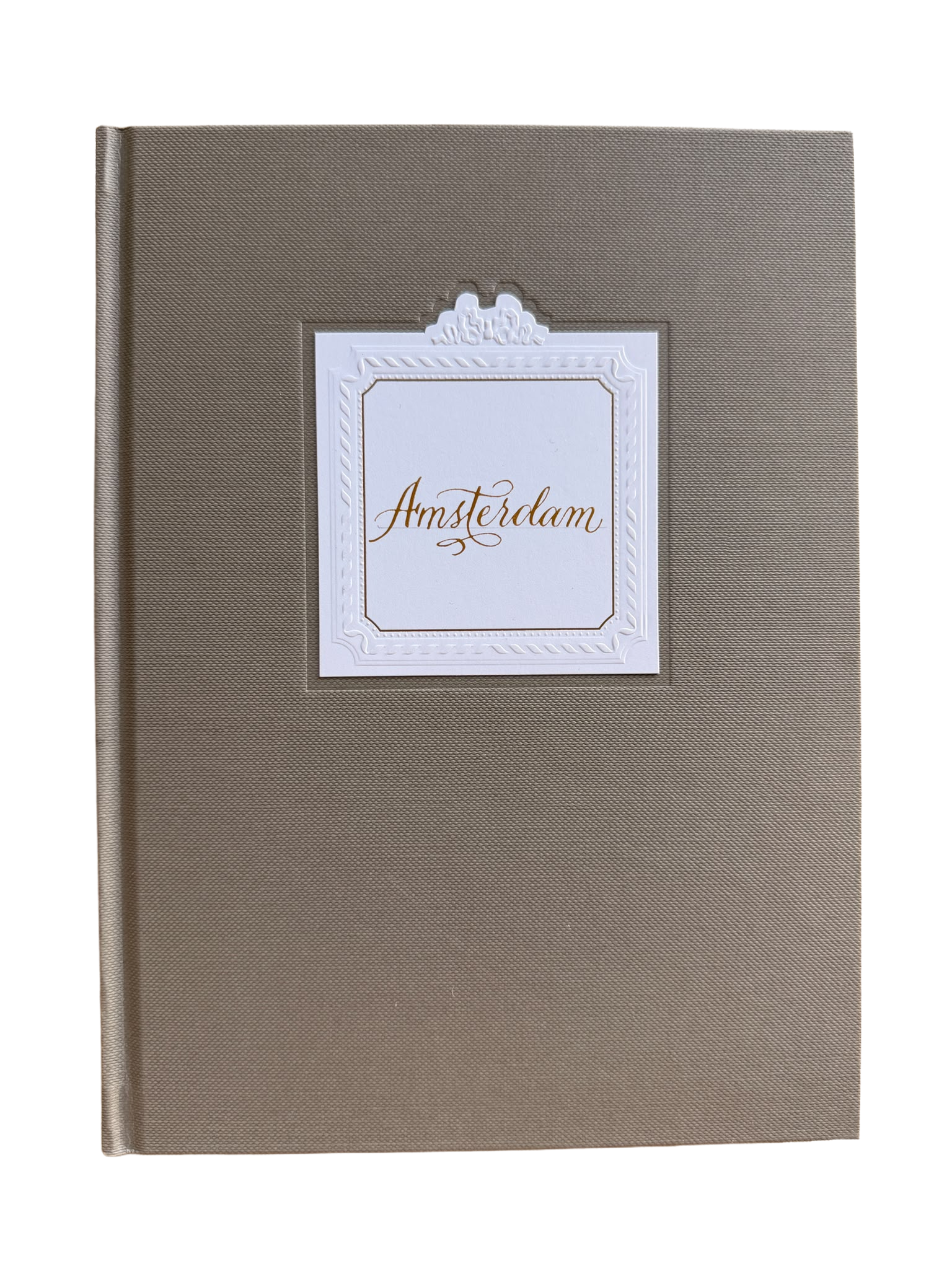 A closed Dior notebook with a white label on the cover that has a decorative border and the word ''Amsterdam'' written in elegant gold script.