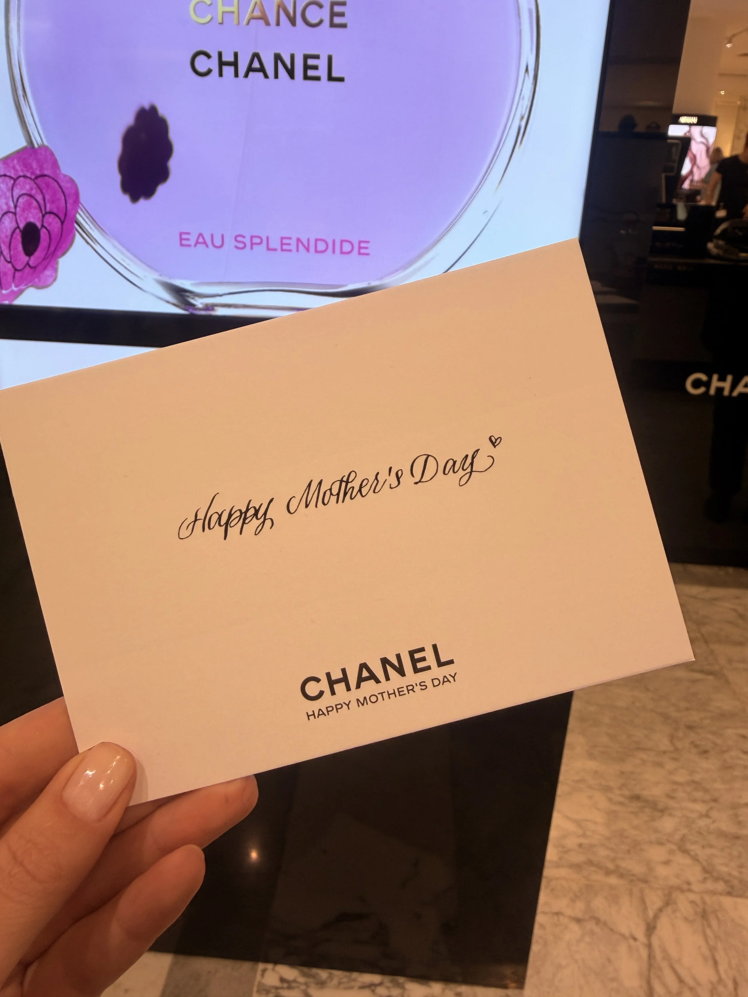 A woman holding a Mother's Day card in front of a display for Chanel Beauty Counter at Bijenkorf in Amsterdam