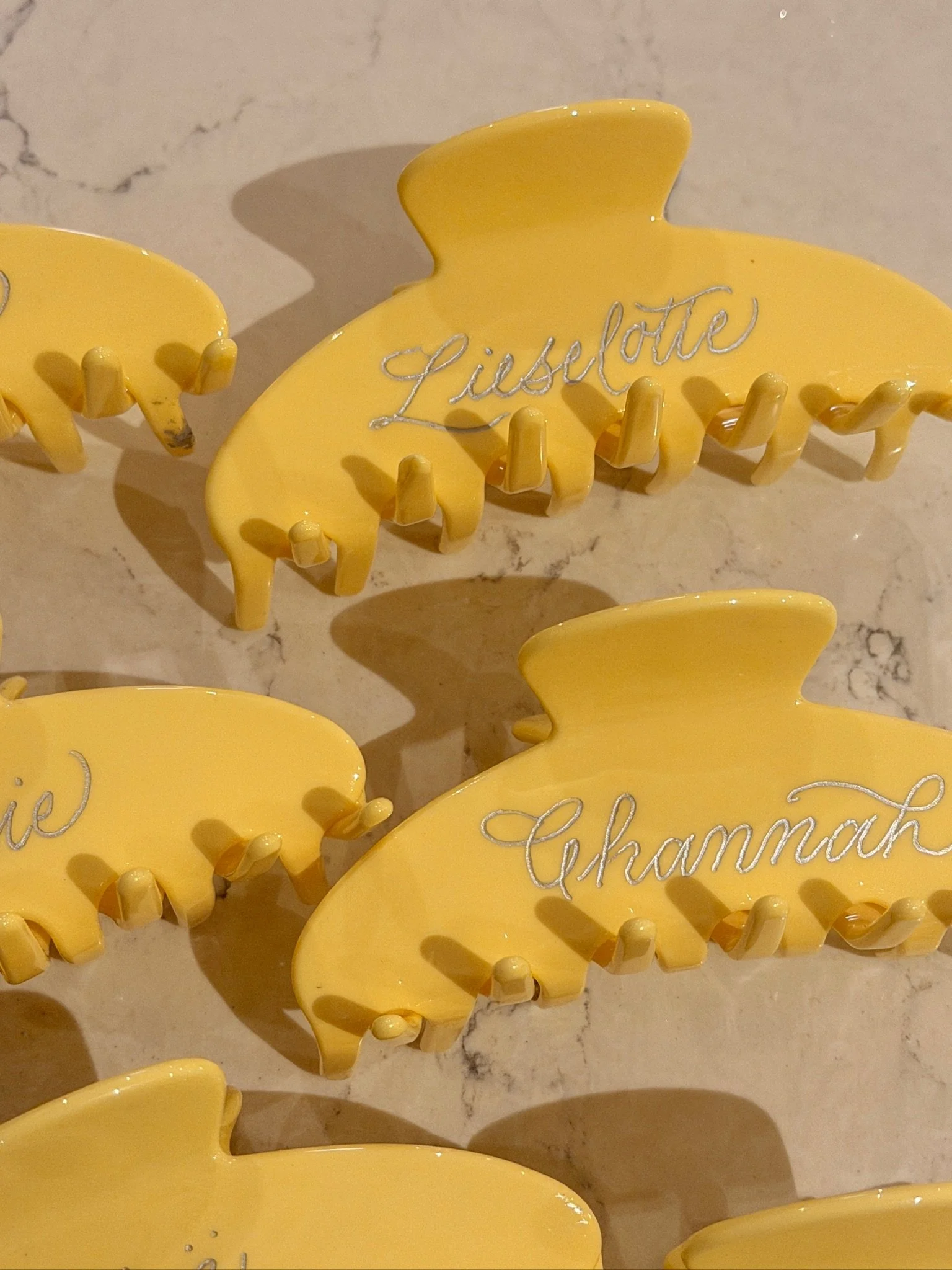 Yellow hair clips with calligraphy engraved, placed on a light marble surface.