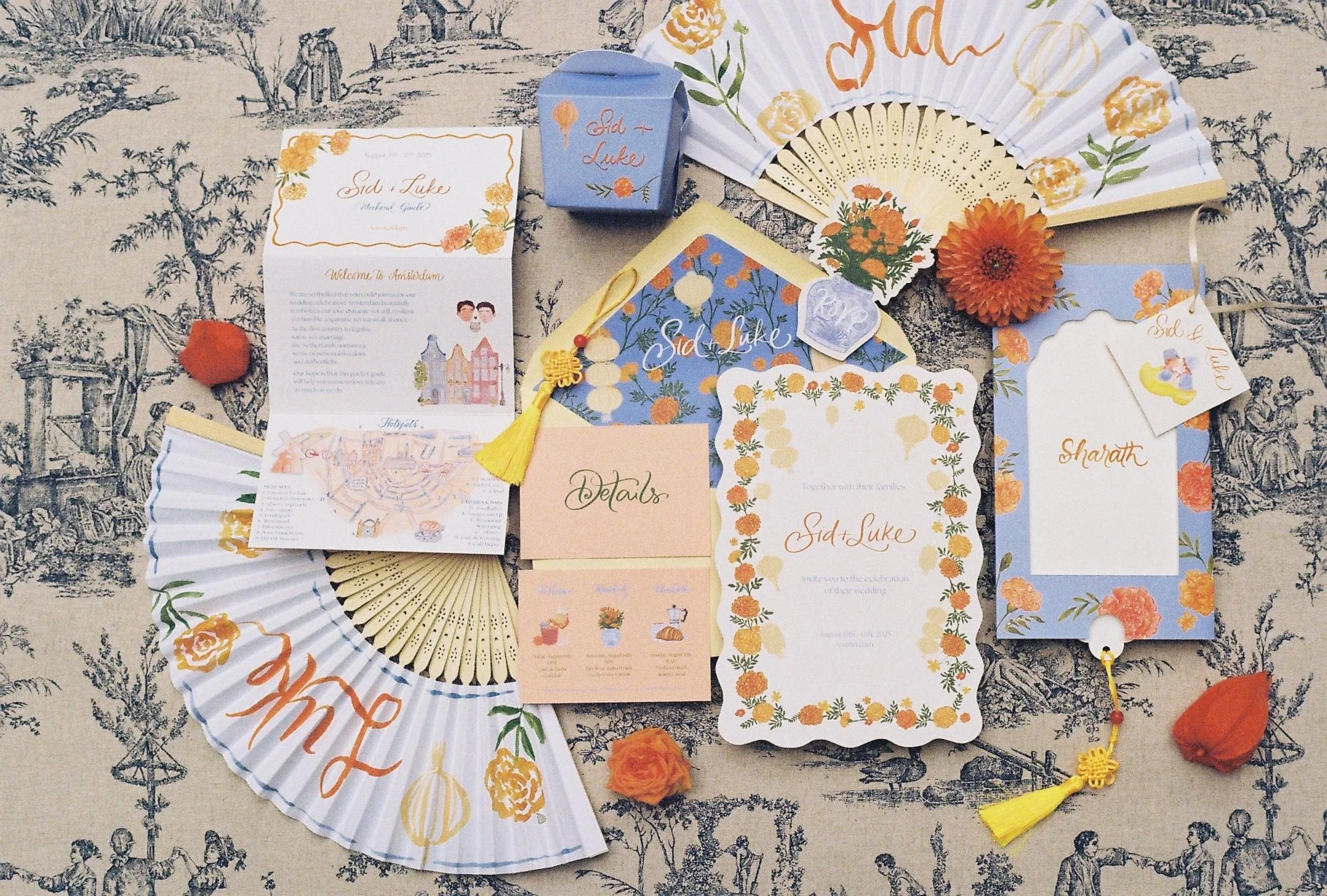 A collection of wedding invitations, cards, and decorations arranged on a decorative fabric surface. The items feature floral and wedding-themed designs in pastel colors, with some including the names 'Sid' and 'Luke'. The arrangement includes fans, 