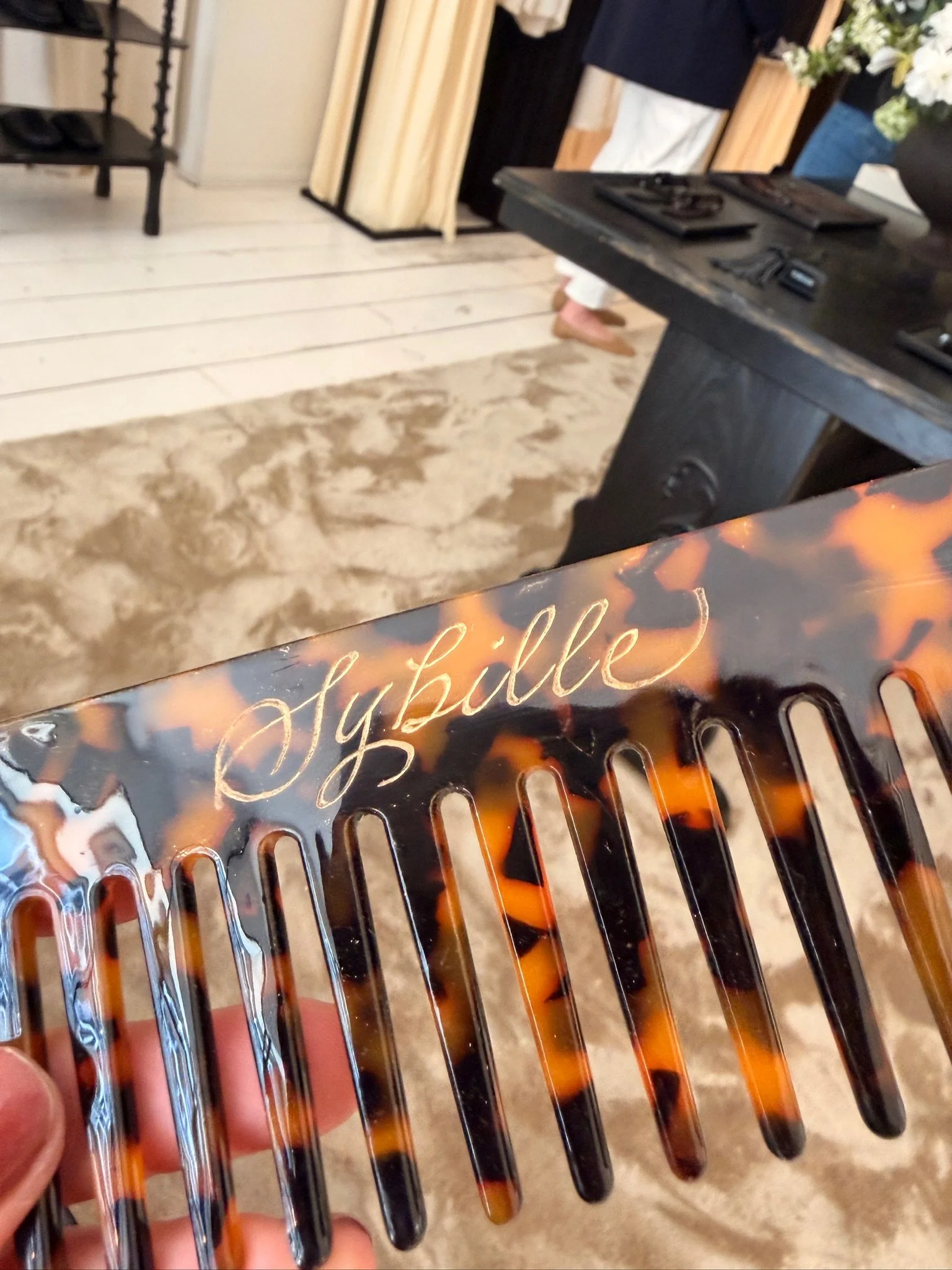 A person's hand holding a tortoise shell pattern hairbrush with the engraved calligraphy name