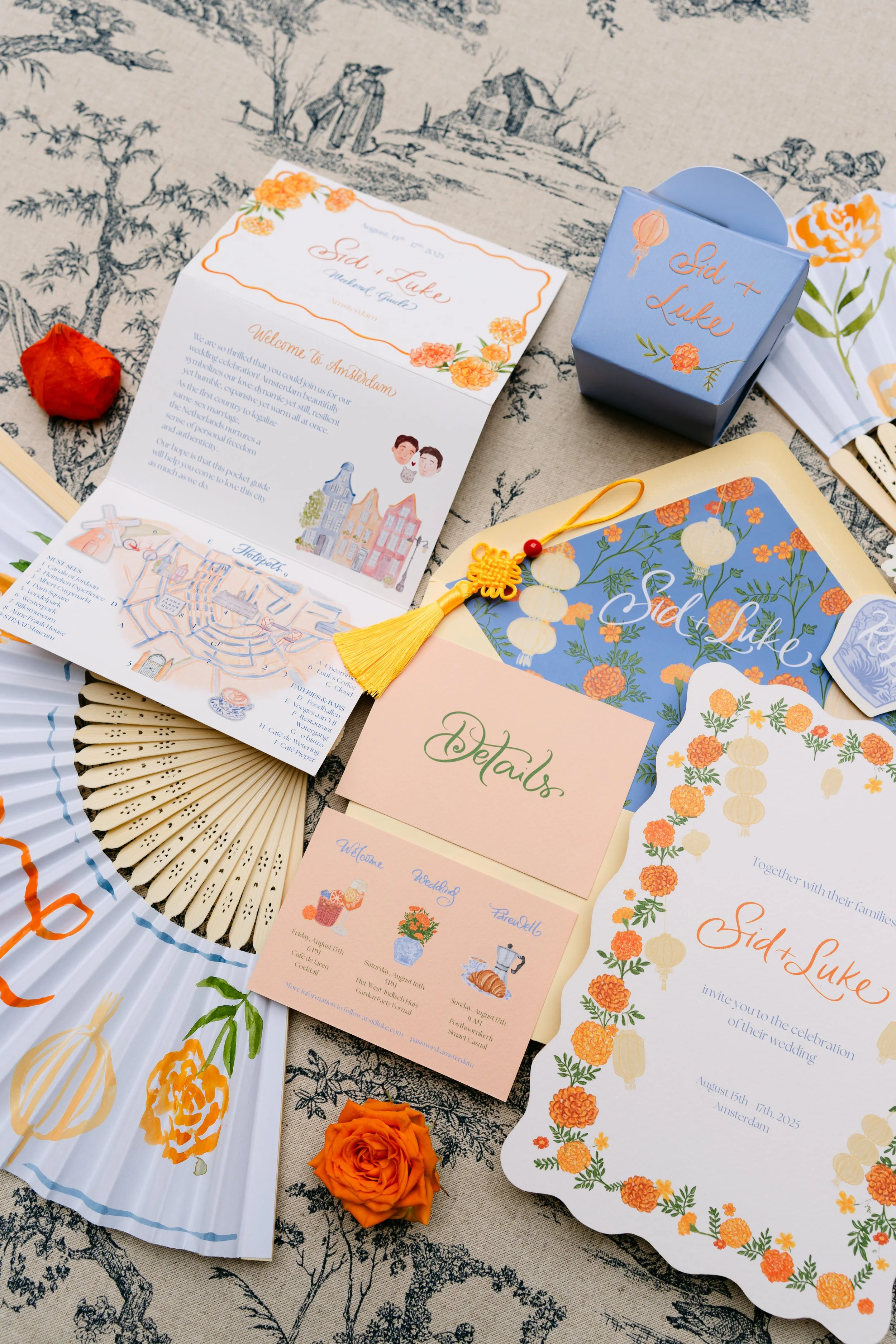Wedding invitation suite and details for Sid and Luke's wedding, including an invitation, RSVP card, and schedule of events, decorated with orange flowers and lantern illustrations, placed on a patterned fabric with orange roses.