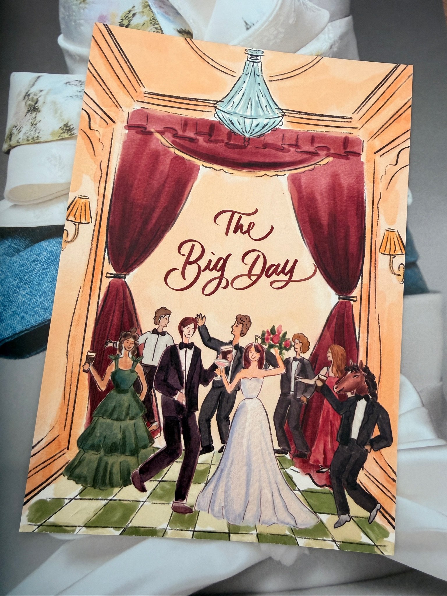 A colorful illustration featuring a group of people celebrating at a wedding reception. The scene is set inside a decorated hall with red curtains, a chandelier, and guests dancing and holding glasses. For Olivia Buckley International.