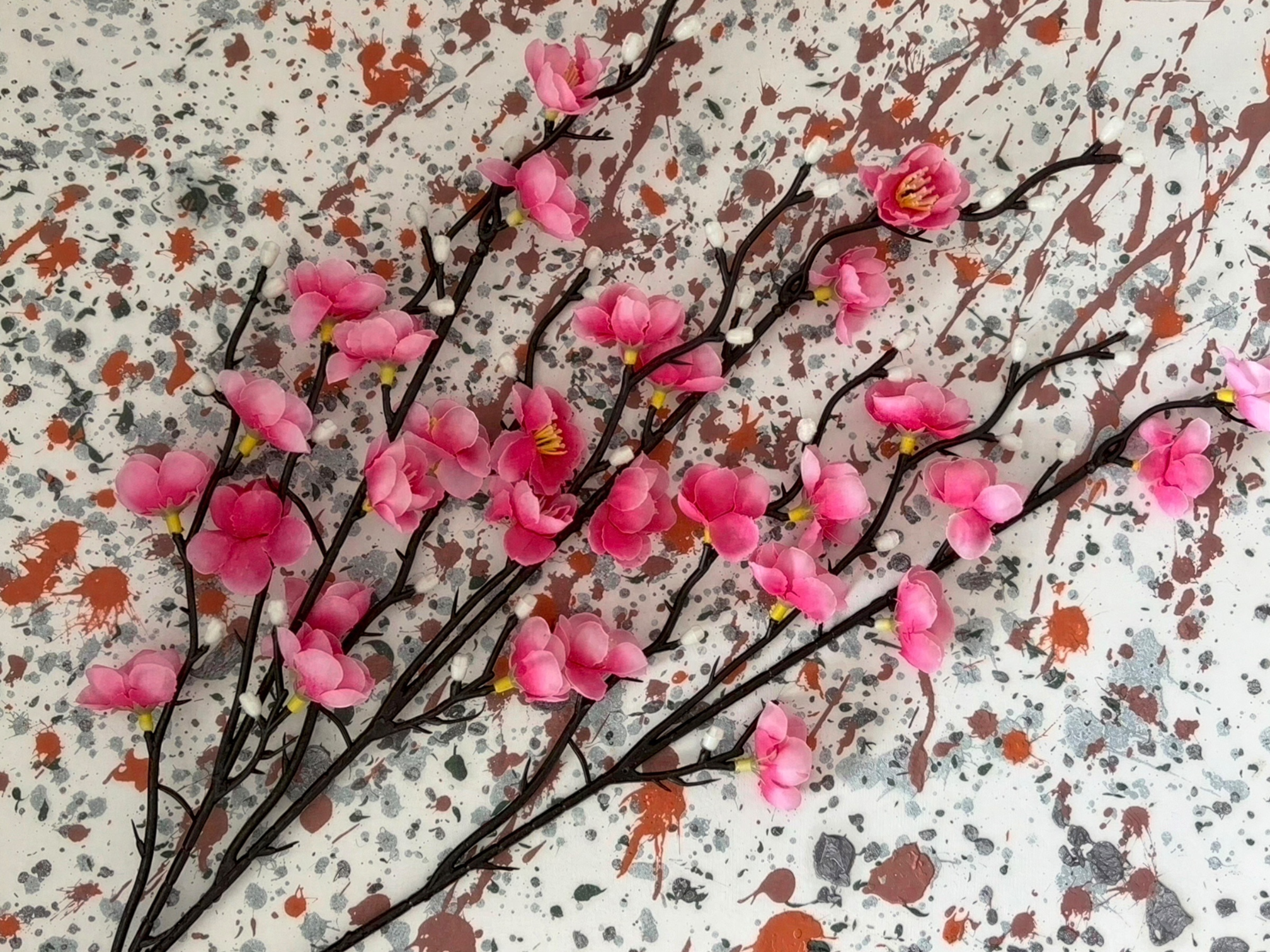 Artificial pink cherry blossom branches on a paint splattered background.