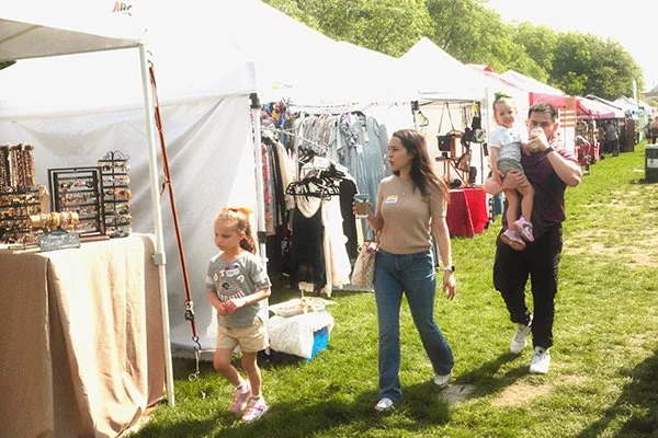People browsing outdoor craft market with tents, racks of clothing, and jewelry displays