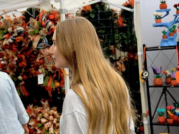 A woman with long blonde hair standing in a store aisle surrounded by decorative wreaths and colorful plant pots.