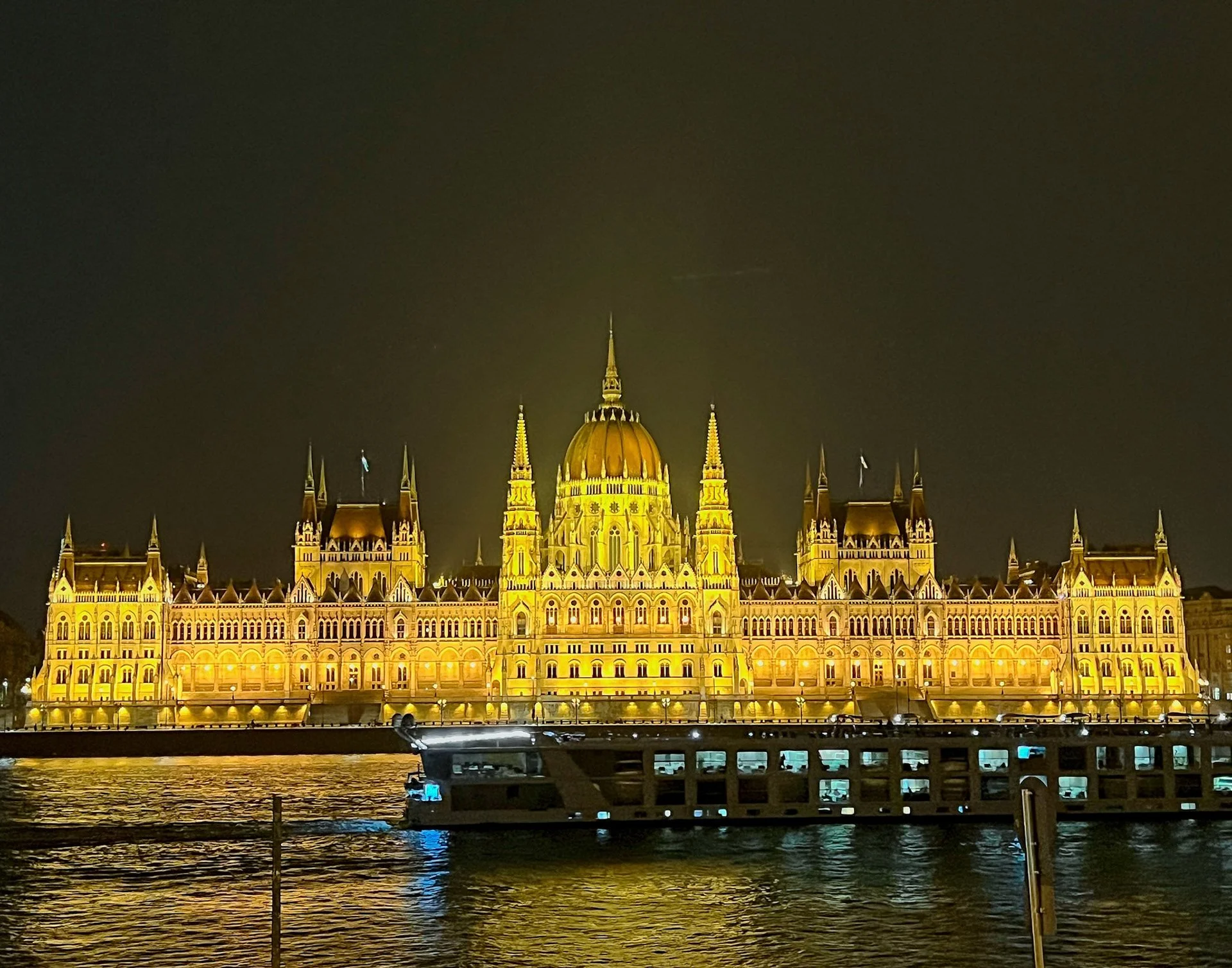 Night view of the illuminated Hungarian Parliament Building with a boat in the foreground on the river.