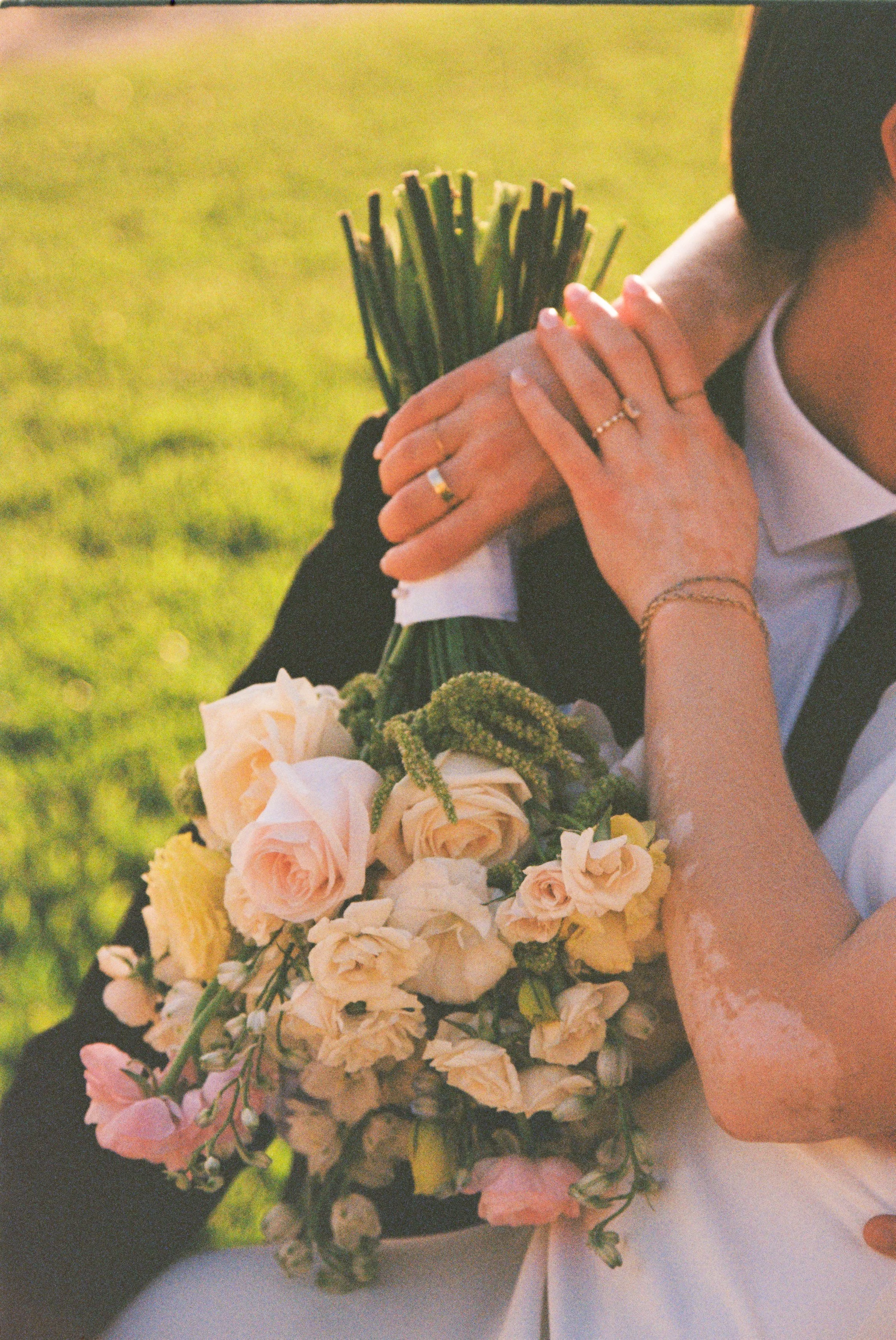Close-up of a person holding a bouquet of flowers and a bundle of green grass, with a blurred green background.