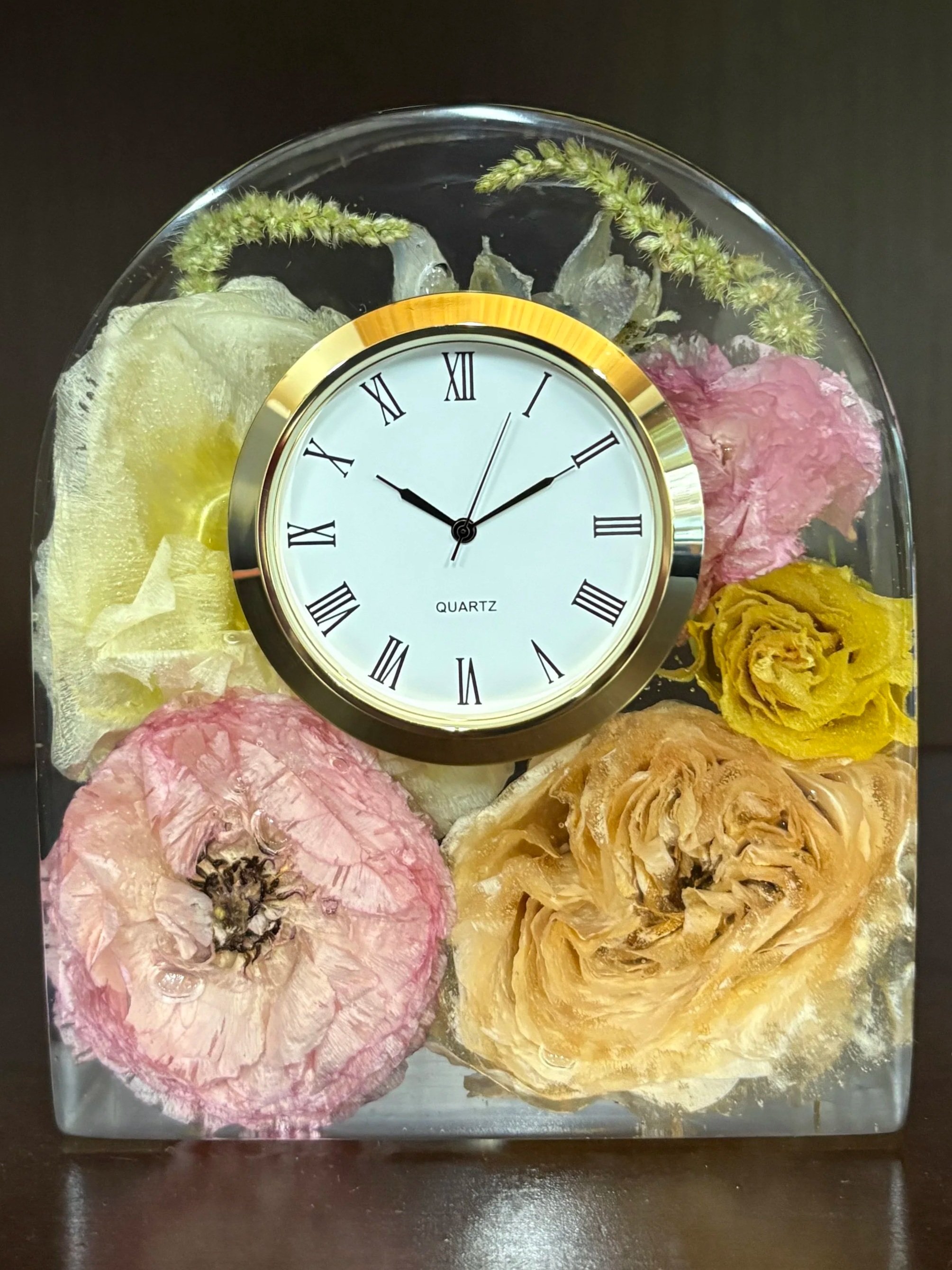 A decorative clock surrounded by dried flower arrangements in shades of pink, yellow, and beige, with some greenery at the back.