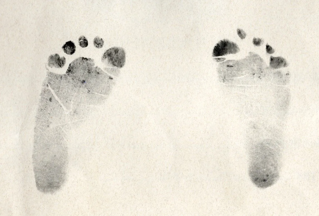 A digital scan of a black-and-white photograph of a baby's footprints from a birth certificate.
