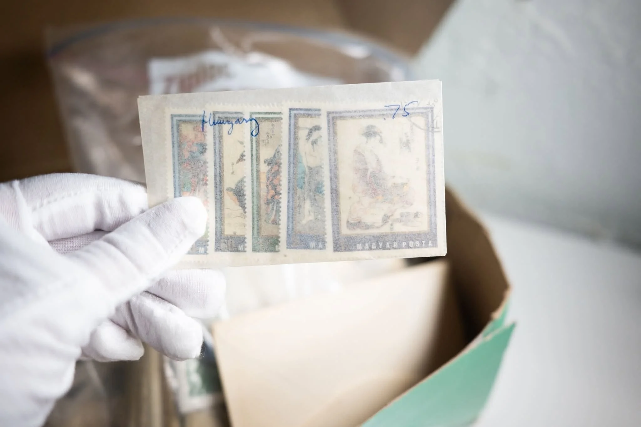 Close-up of a person holding a small sheet of postage stamps with white gloves.