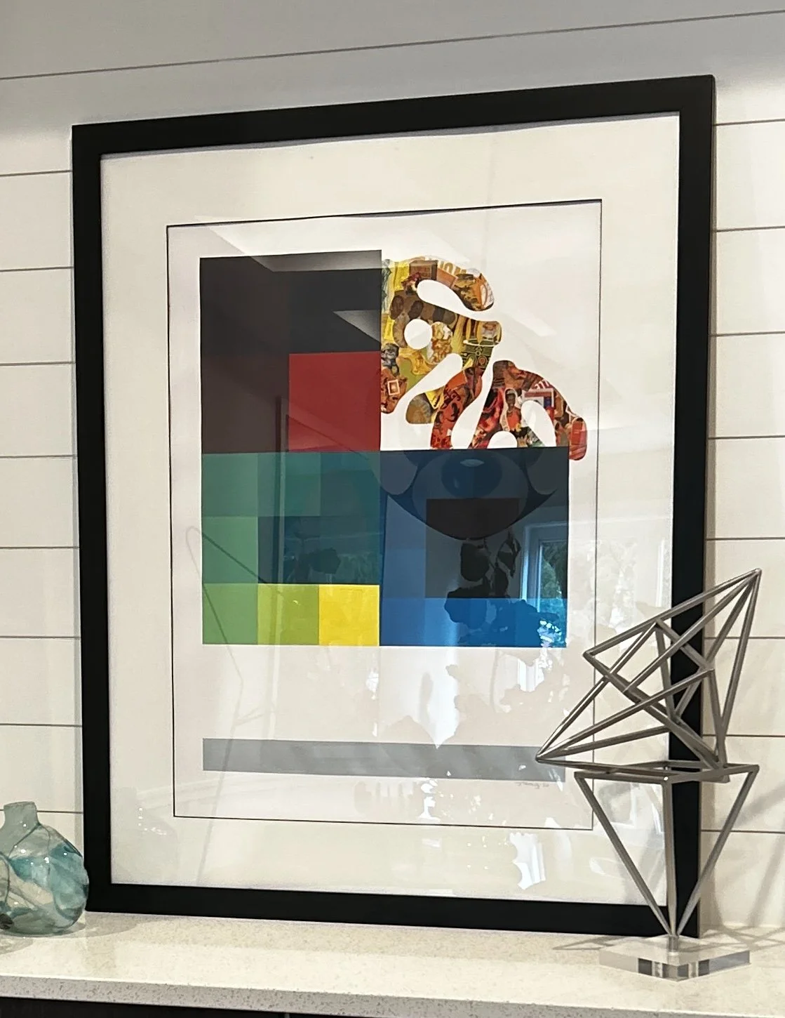 Geometric Abstraction. Decorative framed artwork with colorful geometric shapes and a stylized monkey face, placed on a shelf with decorative vases and a wireframe sculpture.