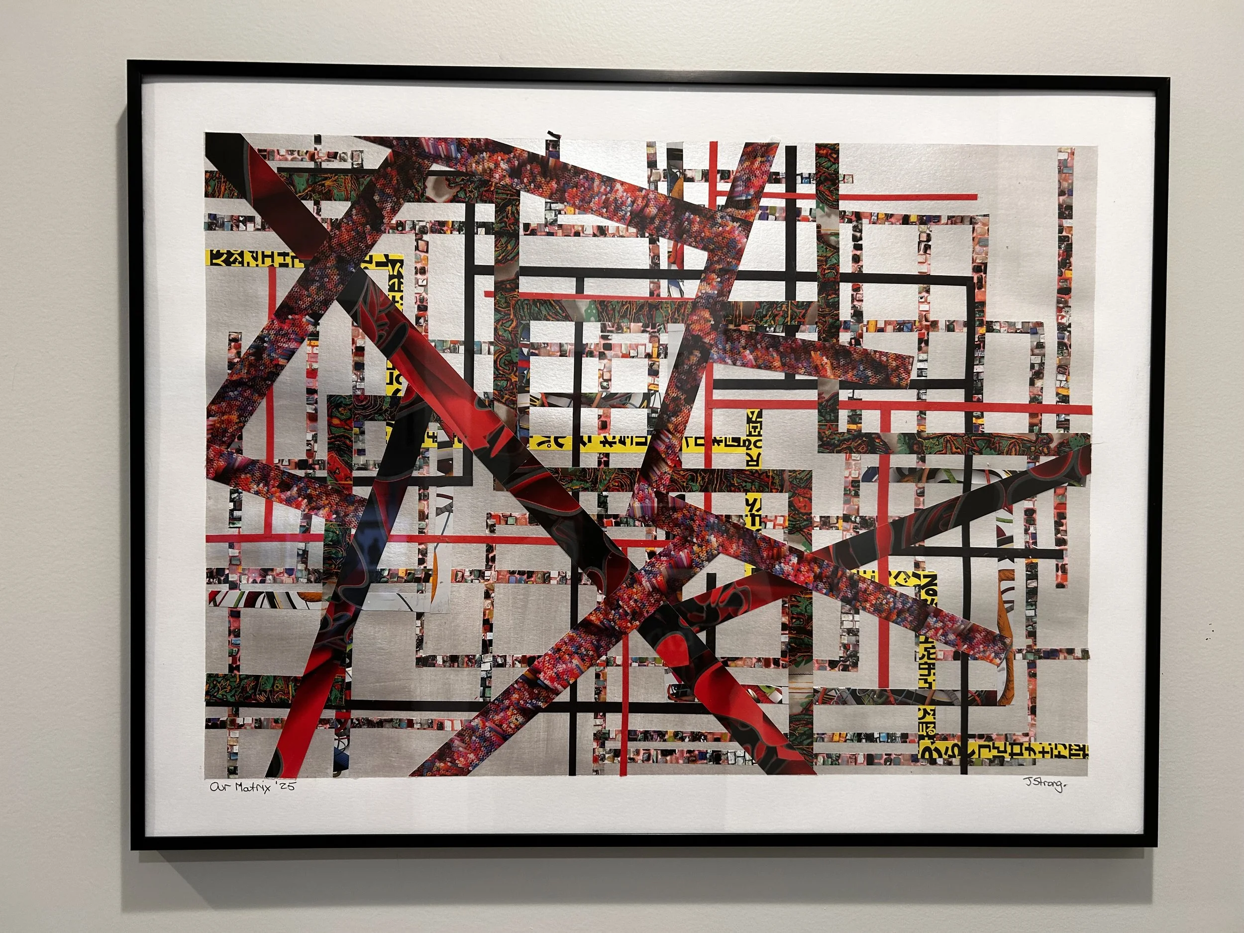 A piece of art titled 'Our Matrix '25' by J. Strang, featuring a collage of various colorful snippets and patterns arranged in a grid with black and red lines, framed and mounted on a white wall.