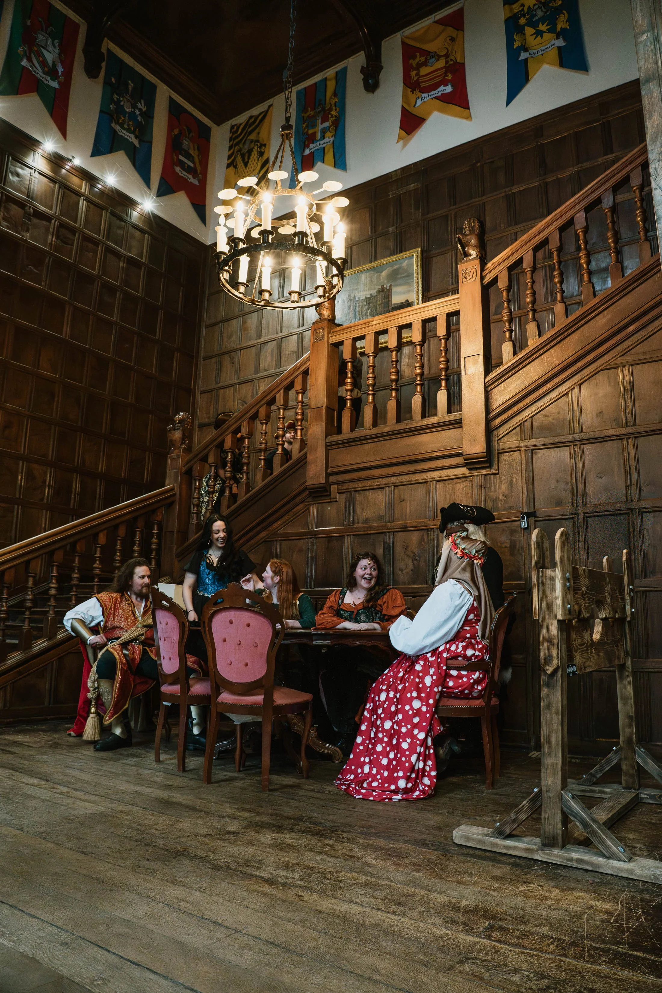People dressed in pirate costumes interacting at a themed event in a wood-paneled room with flags and a chandelier.
