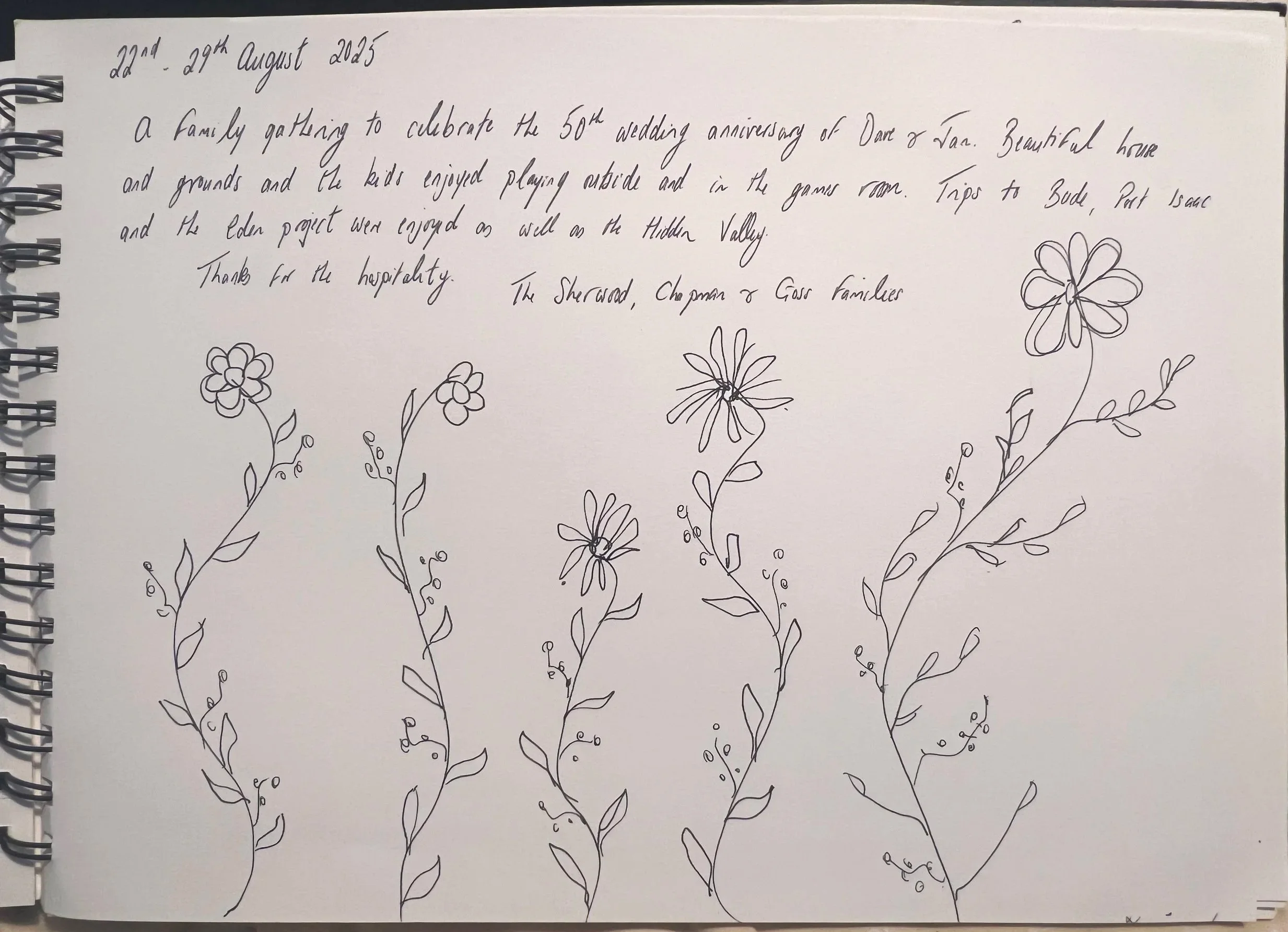 A spiral notebook page with handwritten notes dated August 22-29, 2025, describing a family gathering for a 50th wedding anniversary with garden and outdoor activities. The page features hand-drawn flowers at the bottom at Parnacott house.