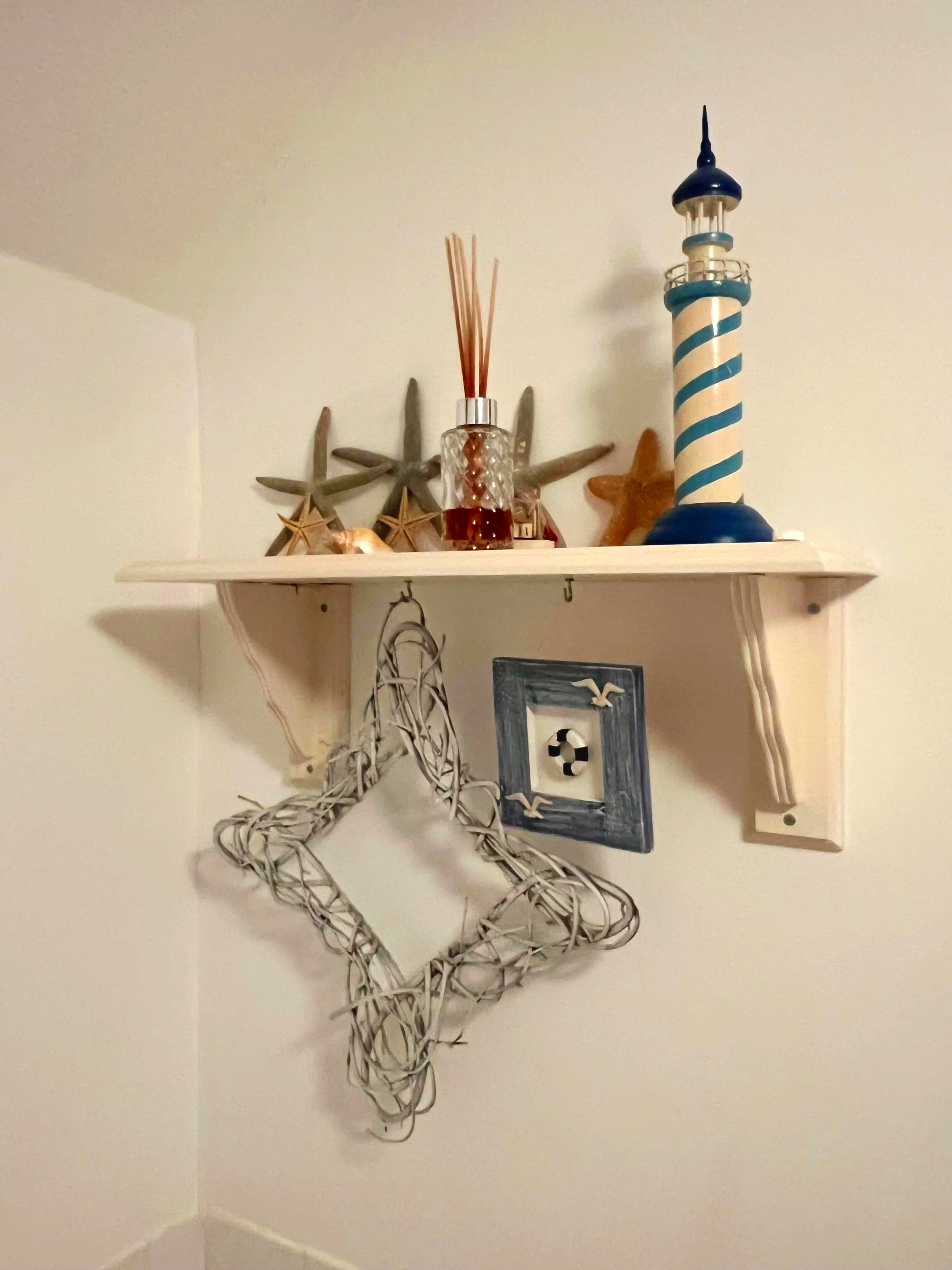 Decorative shelf with starfish, a lighthouse figurine, a glass jar with aroma sticks, and a wooden star. Hanging wire reindeer decoration below the shelf at Parnacott house. 