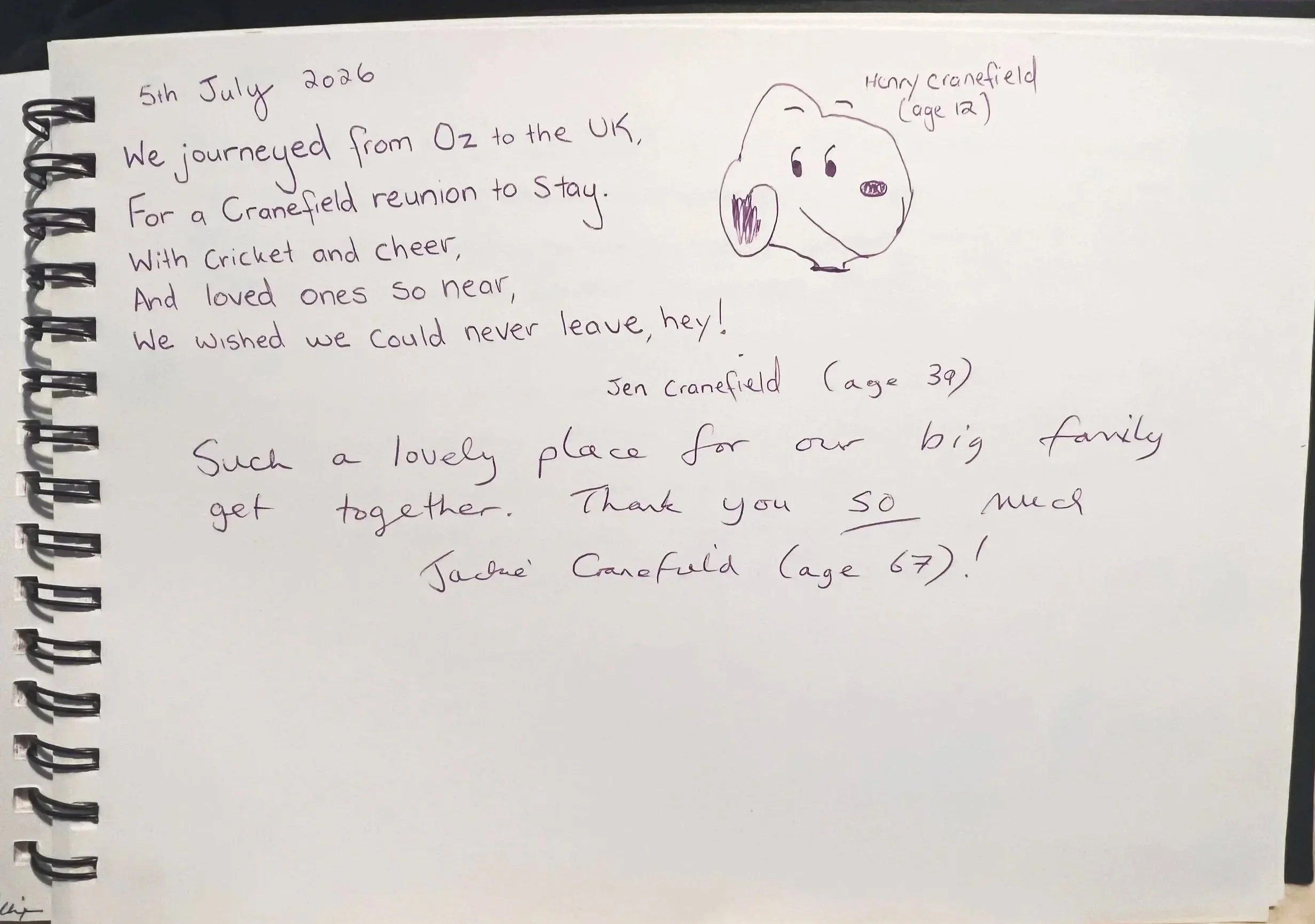 A handwritten note on a spiral-bound notebook page dated July 5, 2026. The note describes a trip from Oz to the UK, a reunion in Cranfield, and a message of love and gratitude from the author and other family members. There is also a simple hand-drawn dog doodle labeled with the name and age 'Henry Cranfield (age 12)' beside it.