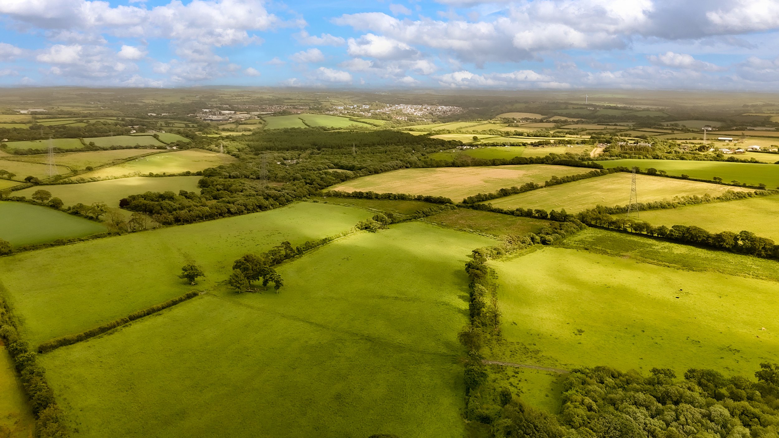 Aerial view of rolling green fields, patches of forest, and farmland under a partly cloudy sky at Parnacott house.