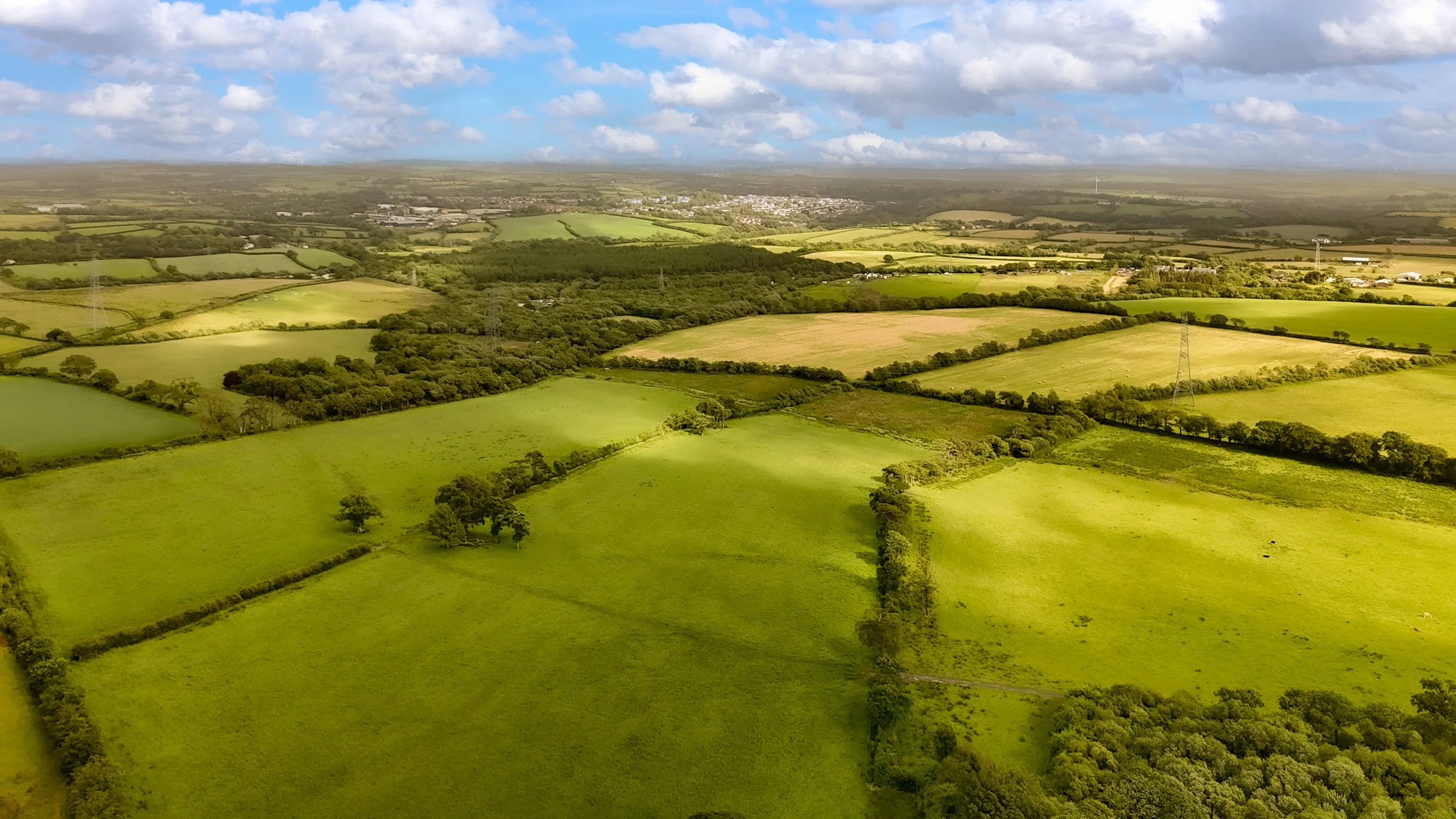 Aerial view of green farmland with patches of trees and fields under a partly cloudy sky at Parnacott house.