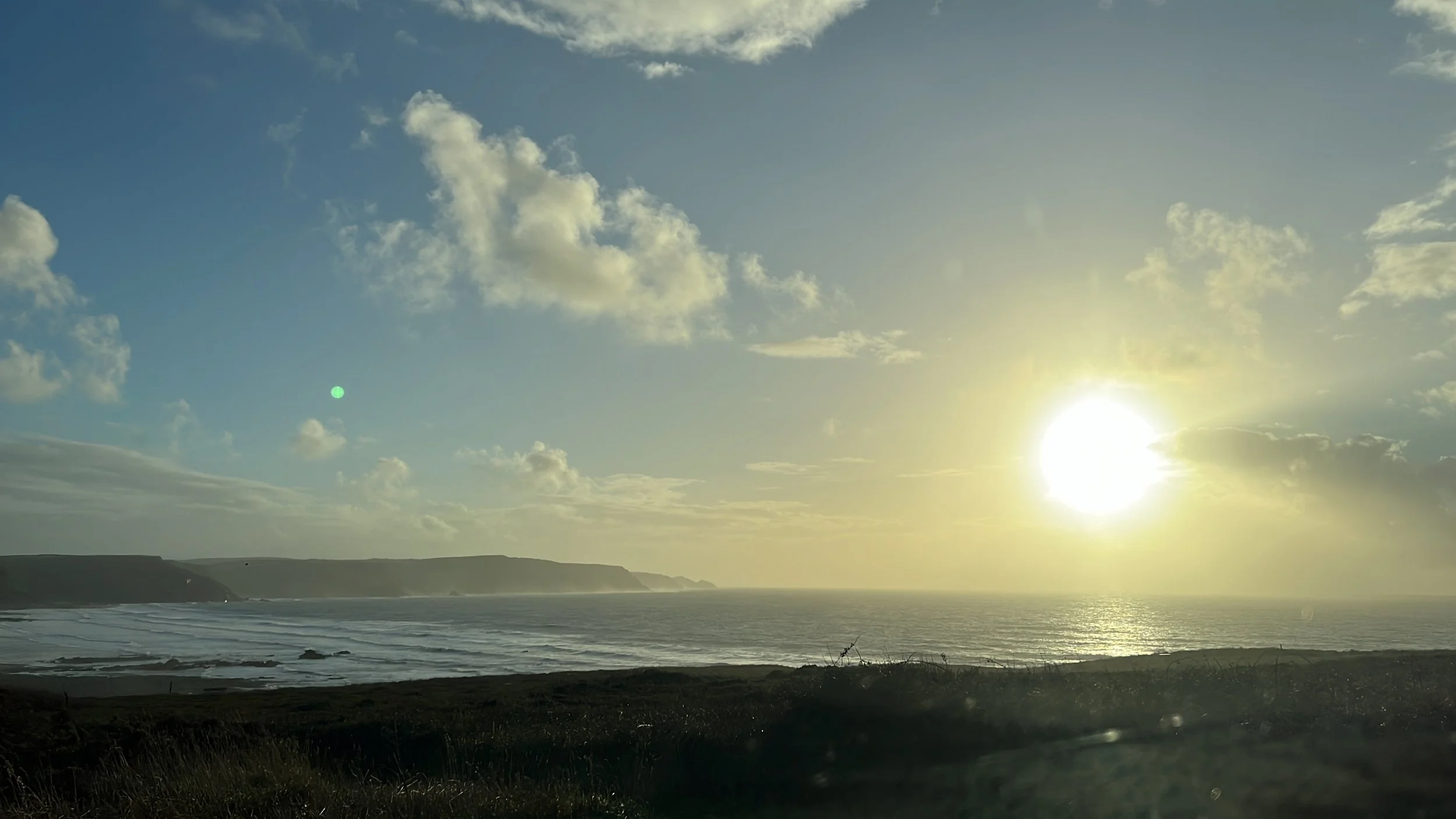 Sunset over the ocean with clouds in the sky and a coastline in the distance at Parnacott house.