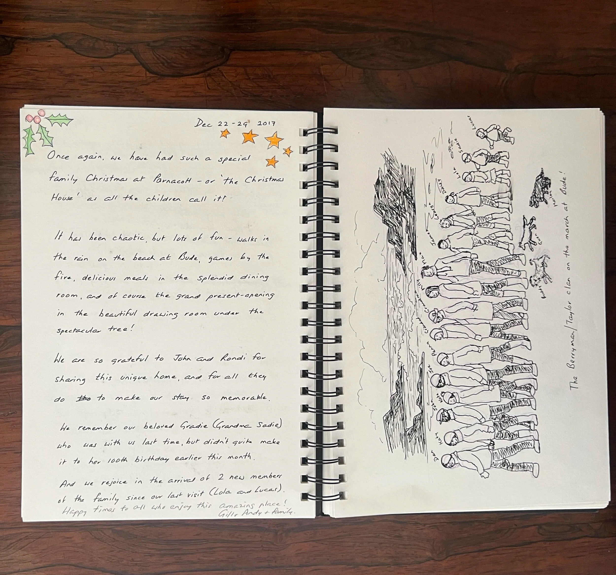 Open spiral notebook on a wooden surface showing handwritten and illustrated holiday and family memories, including Christmas scenes, family photos, and personal notes at Parnacott house.