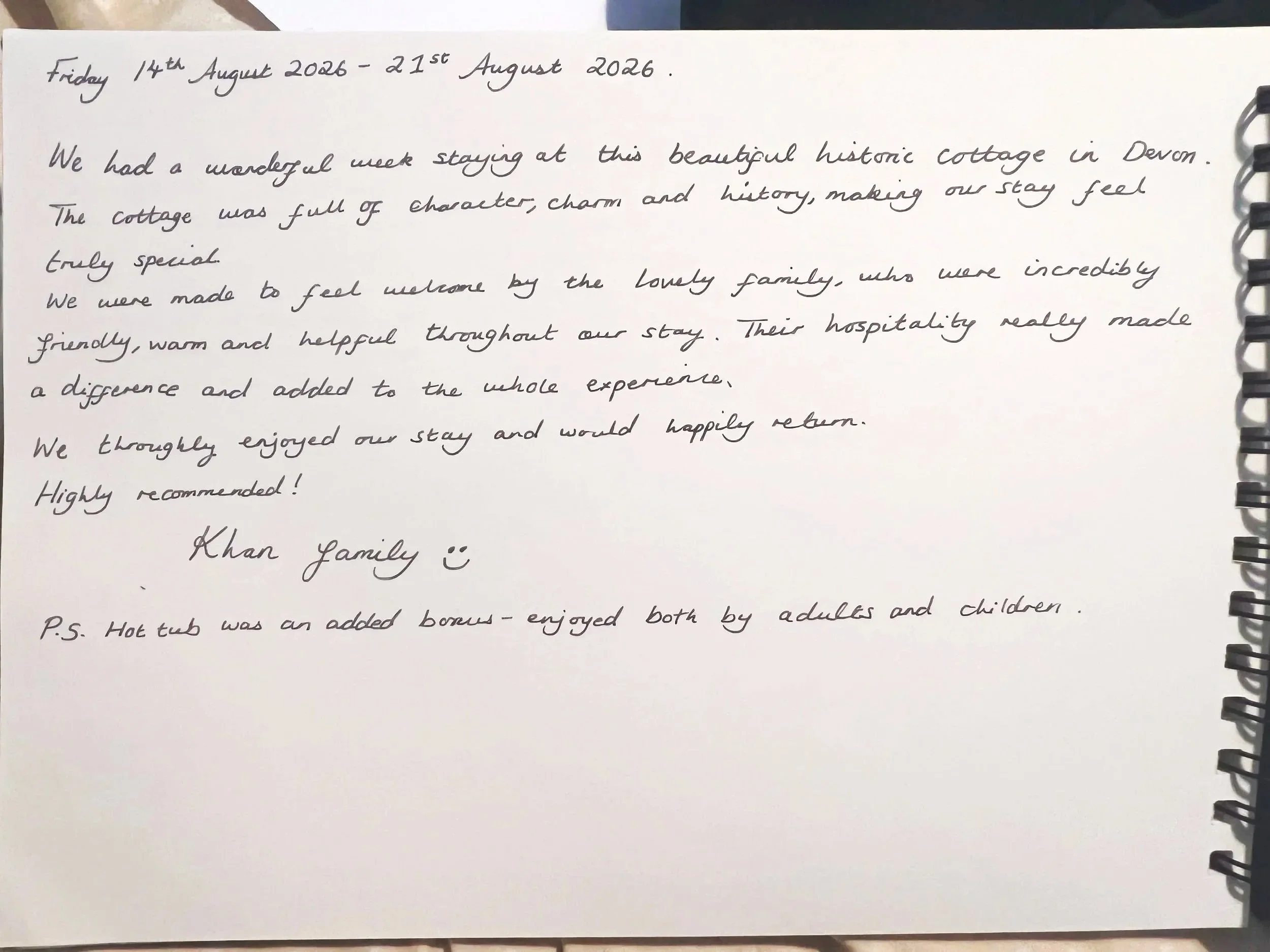 A handwritten note on a white spiral notebook page, dated August 14th and 21st, 2026. The note describes a week's stay at a historic cottage in Devon, highlighting the charm, hospitality, and experiences of the family that hosted them at Parnacott.