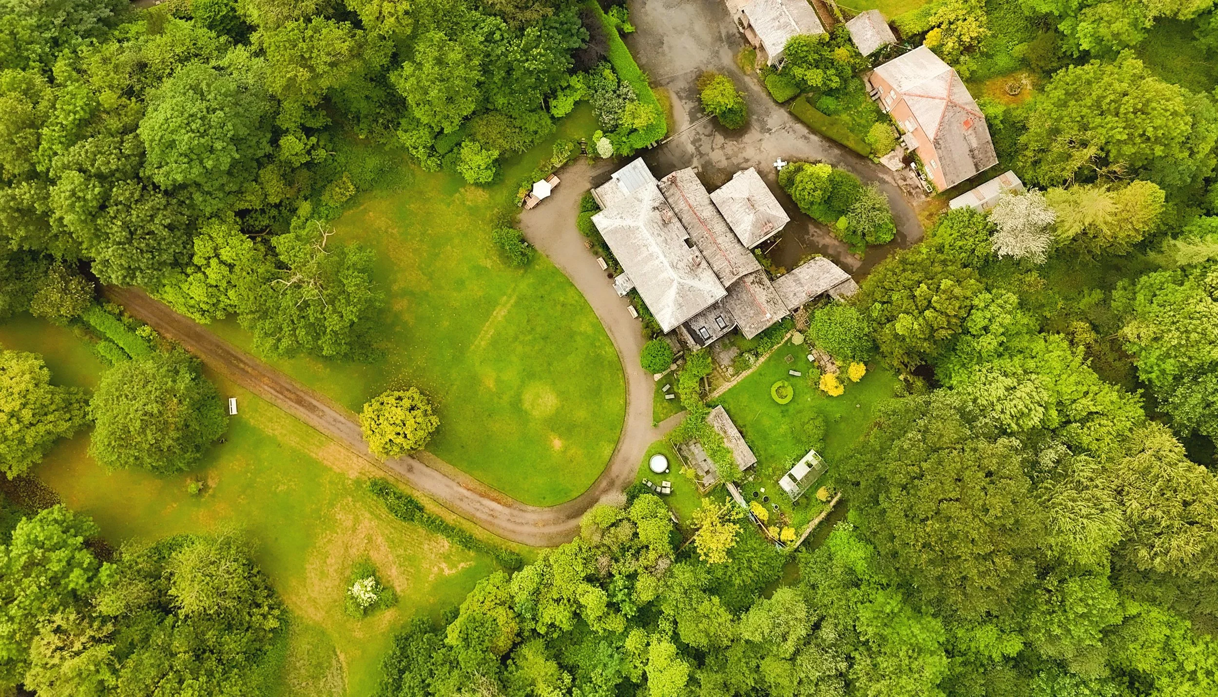 Aerial view of a large house surrounded by dense green trees and a grassy yard with walking paths at Parnacott house.