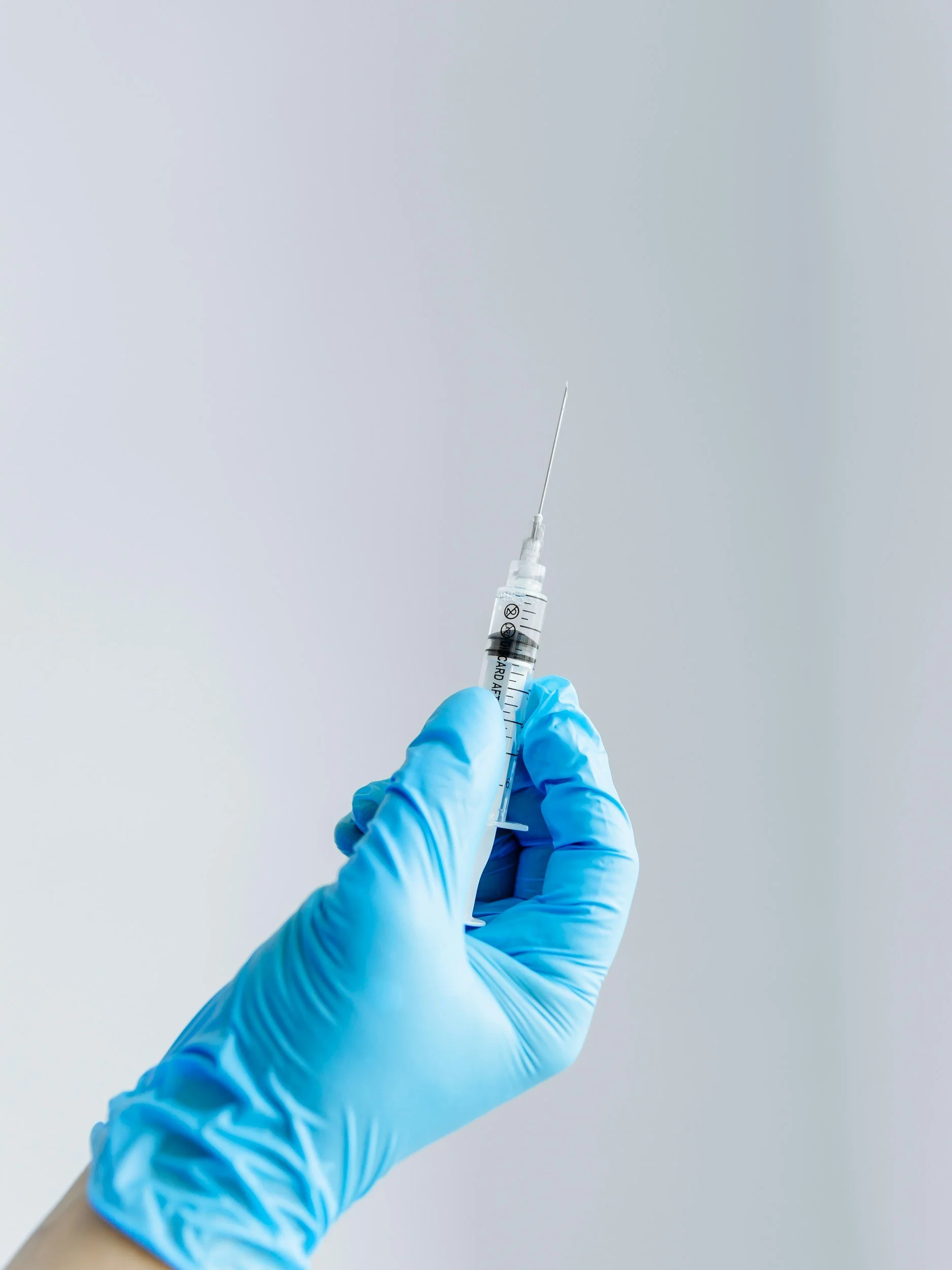 A healthcare professional wearing blue gloves holding a syringe with a needle against a plain background.