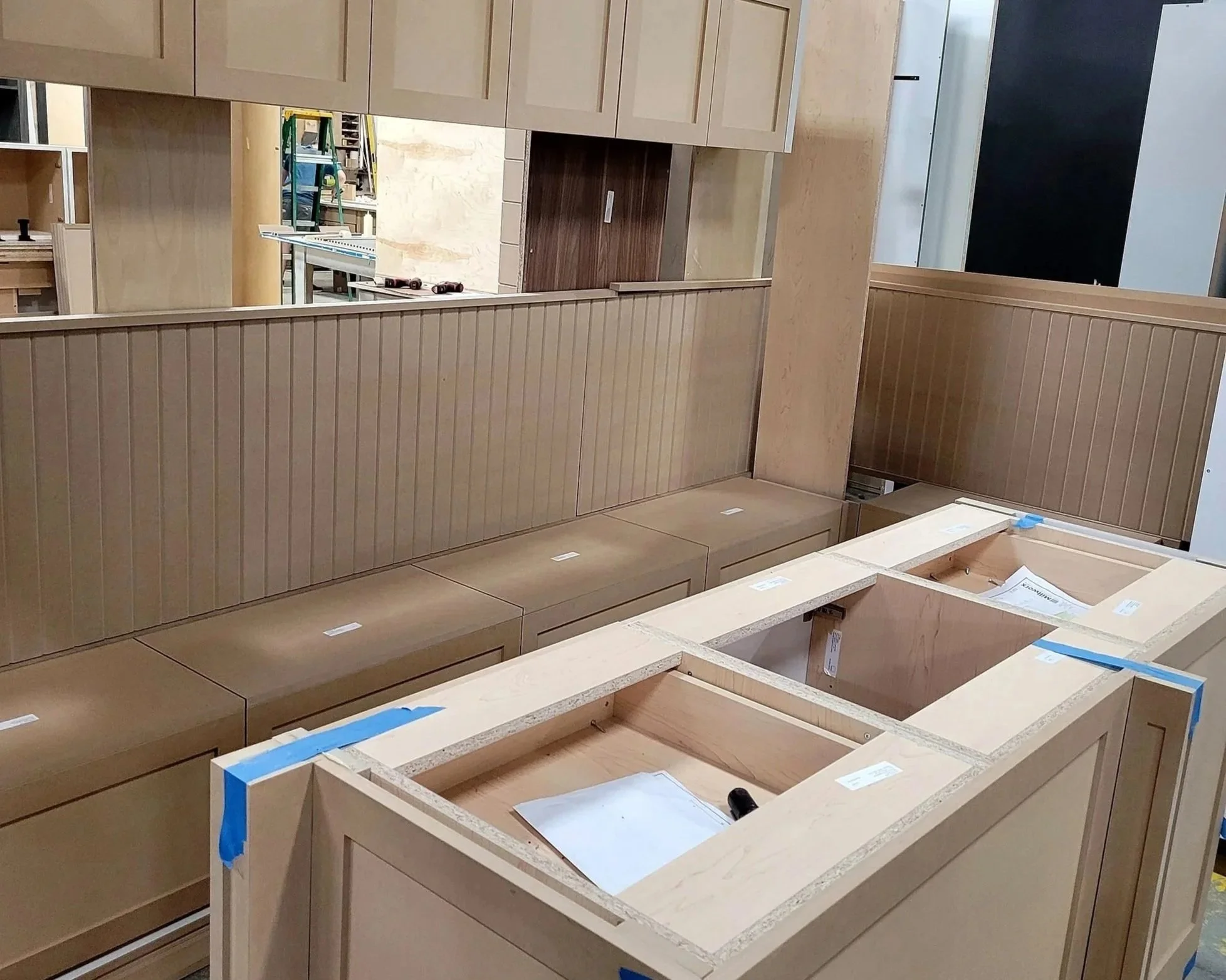 Wooden kitchen cabinets and countertops under construction, with tools and blue painter's tape.