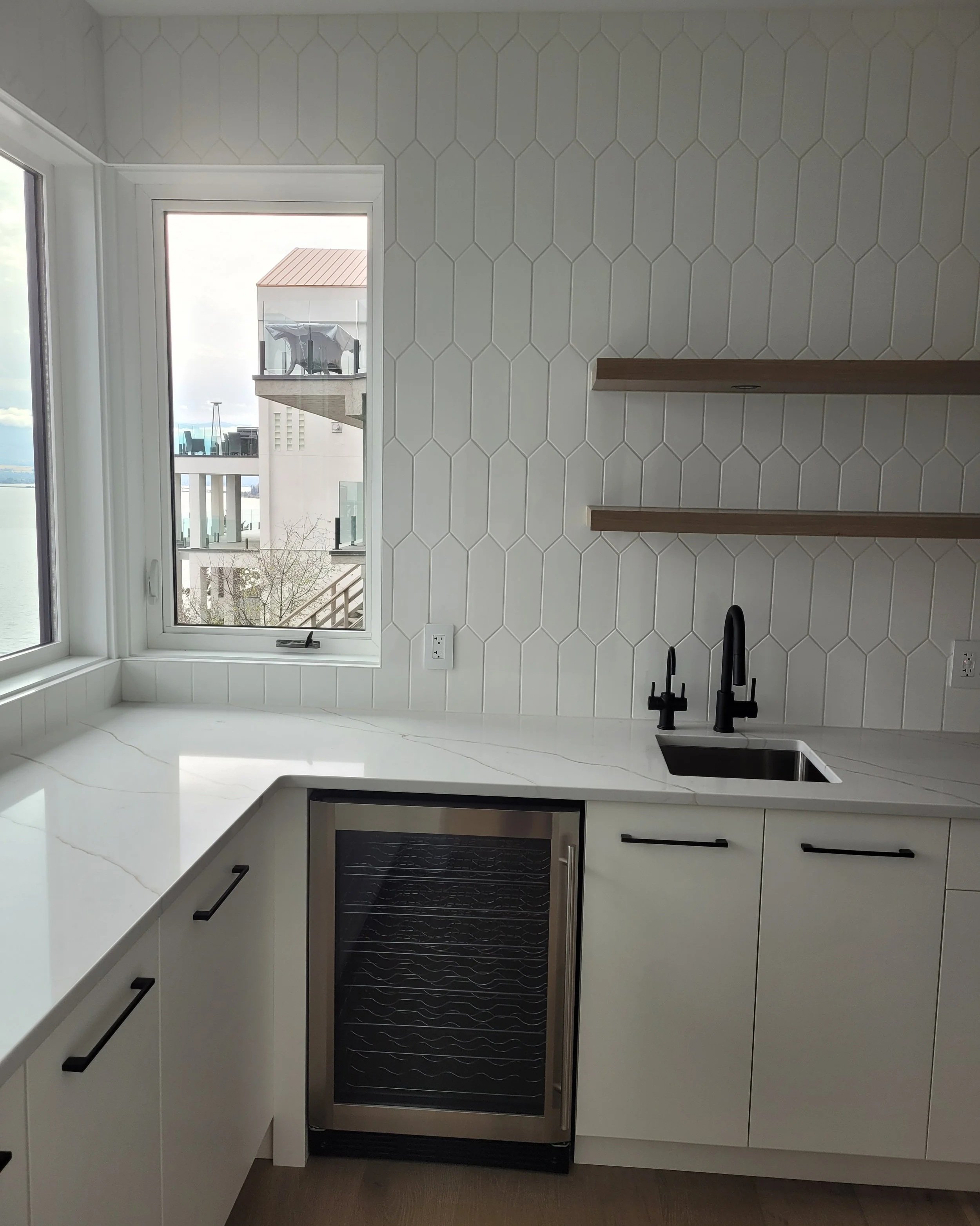 Modern kitchen with a white countertop, black faucet, built-in oven, white cabinets, and a window showing balcony with outdoor furniture.