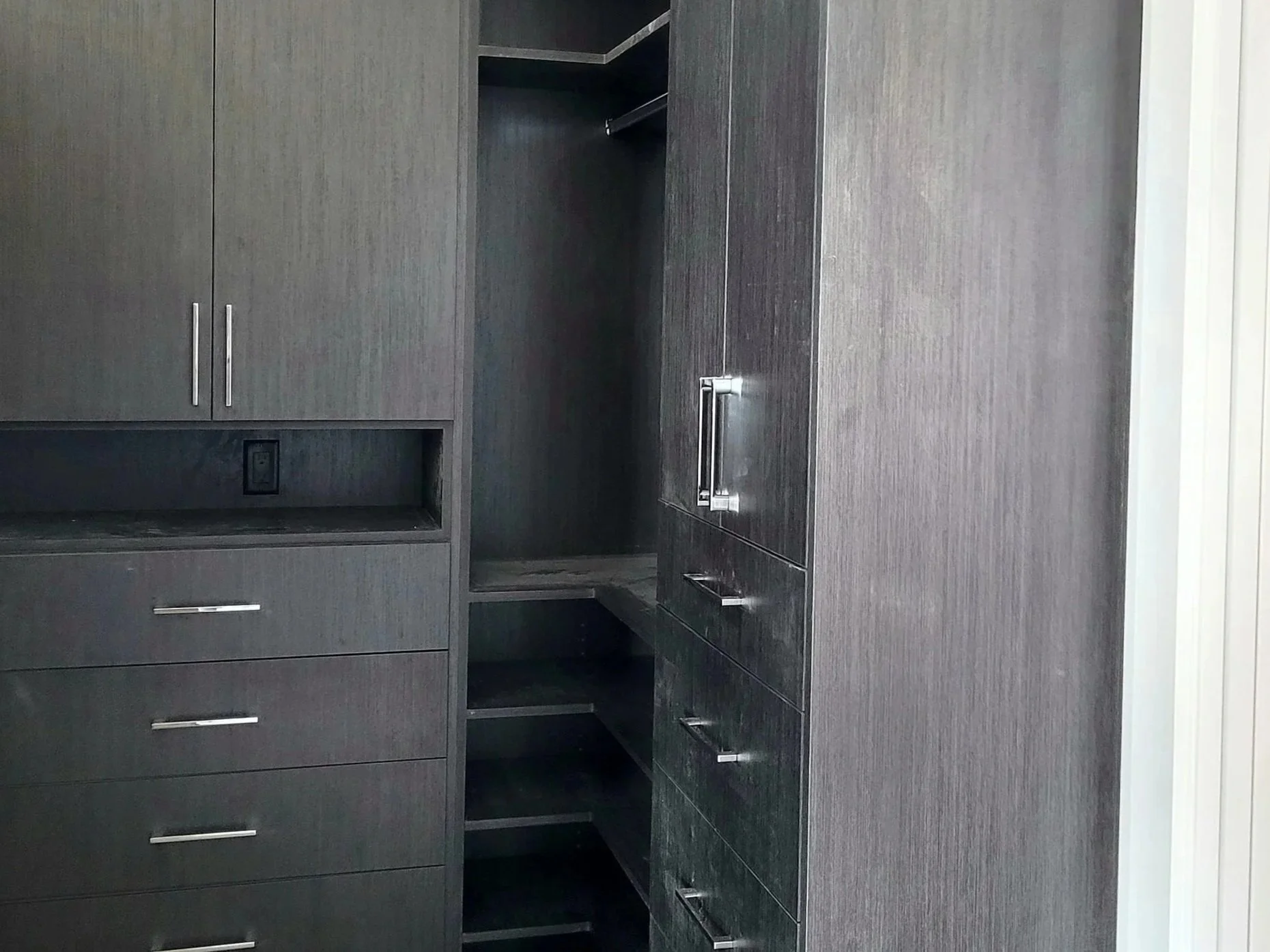 Interior of a dark gray closet with shelves and drawers, some open showing storage space, and silver handles on the doors.