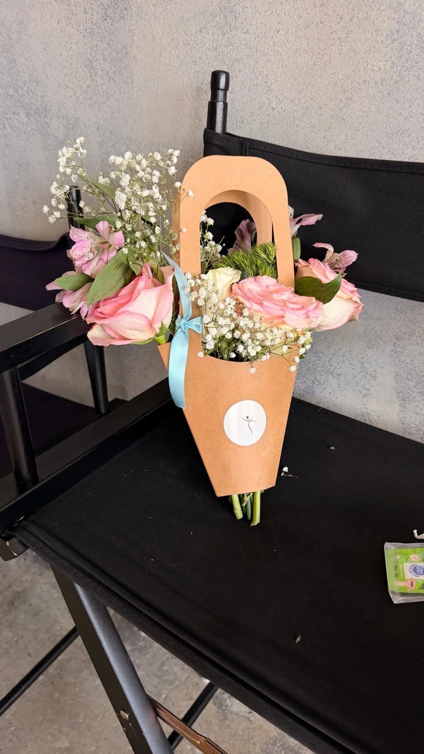 Pink and ivory bouquet in a personalized kraft flower bag with blue ribbon at a BloomMuseCo event