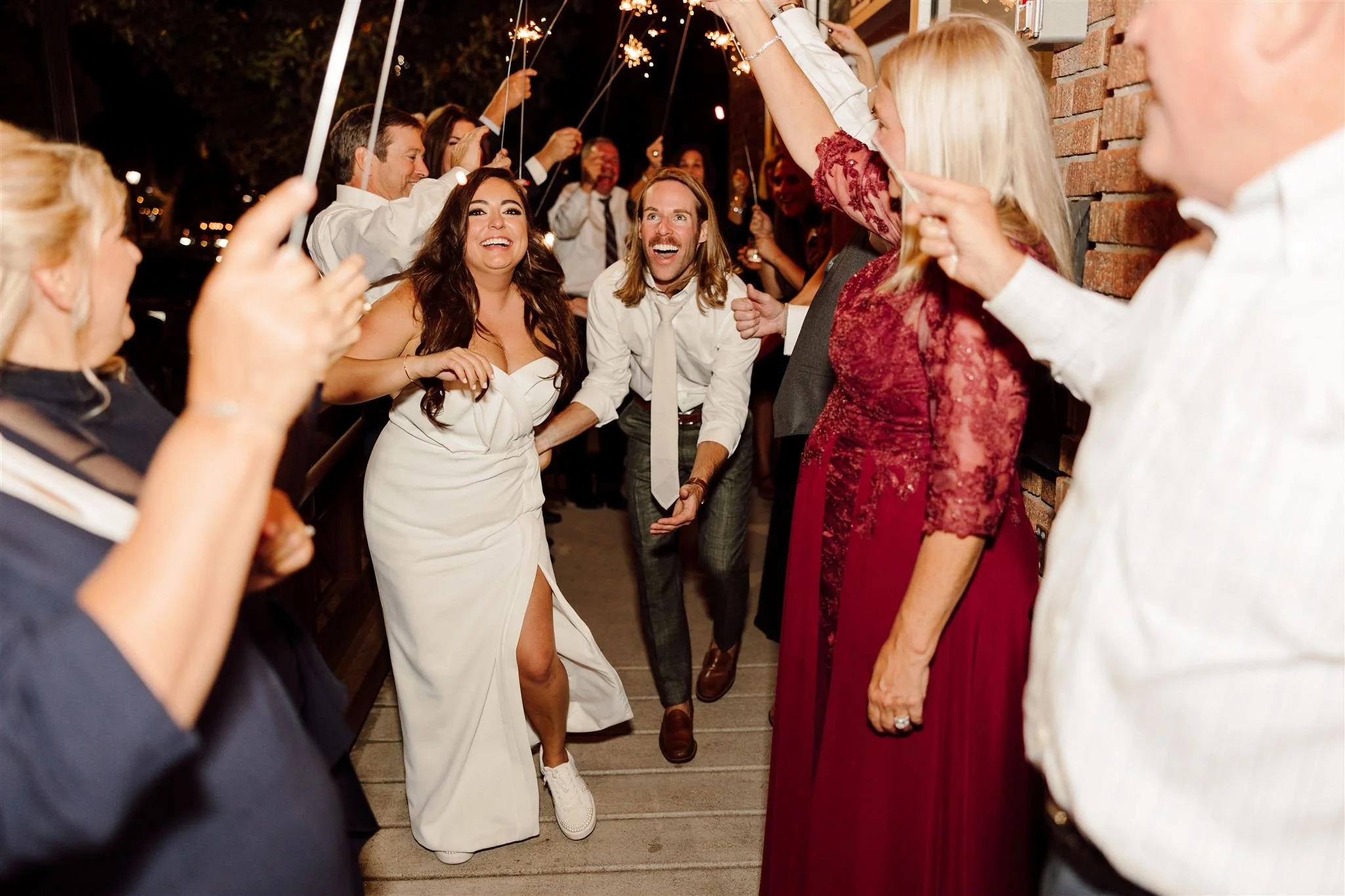 A group of people celebrating at night, holding sparklers while a woman in a white dress dances and smiles in the center.