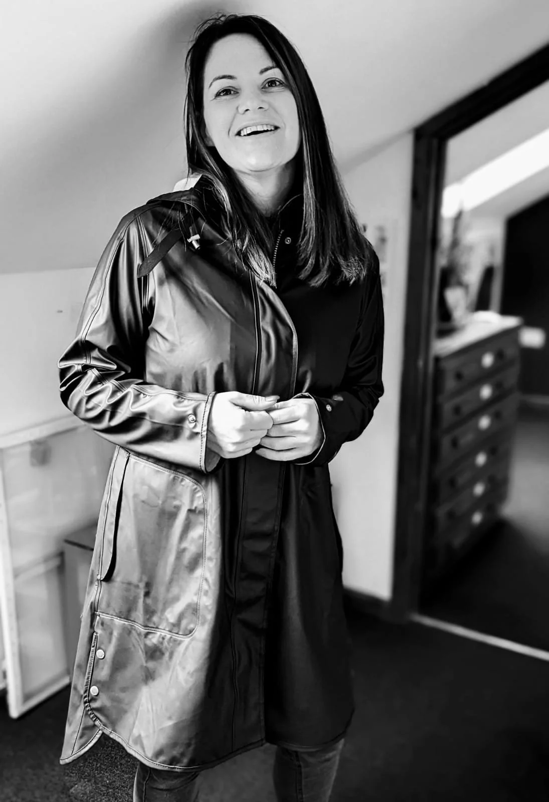 A black and white picture of Louise McLoughlin smiling, standing in her happy place, her art studio