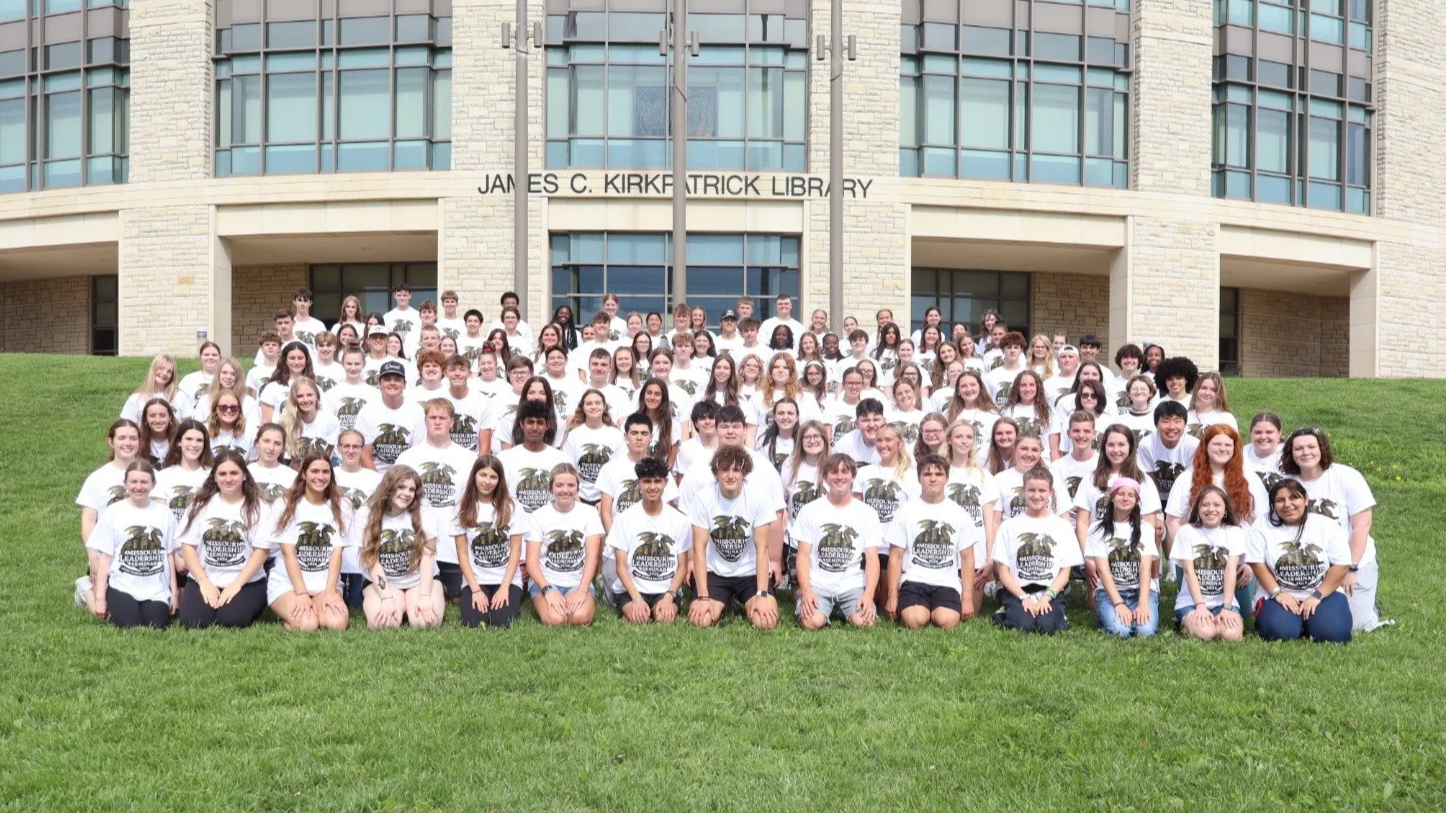 Large student group posing on the lawn outside the James C. Kirkpatrick Library.