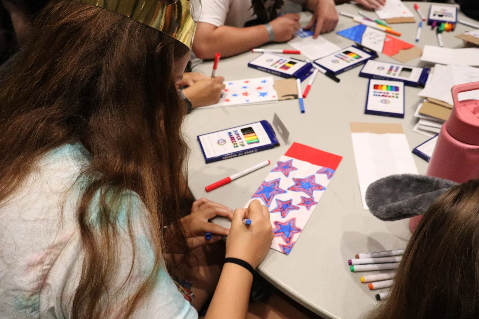 Children decorate star-patterned artwork with colorful markers at a craft table.