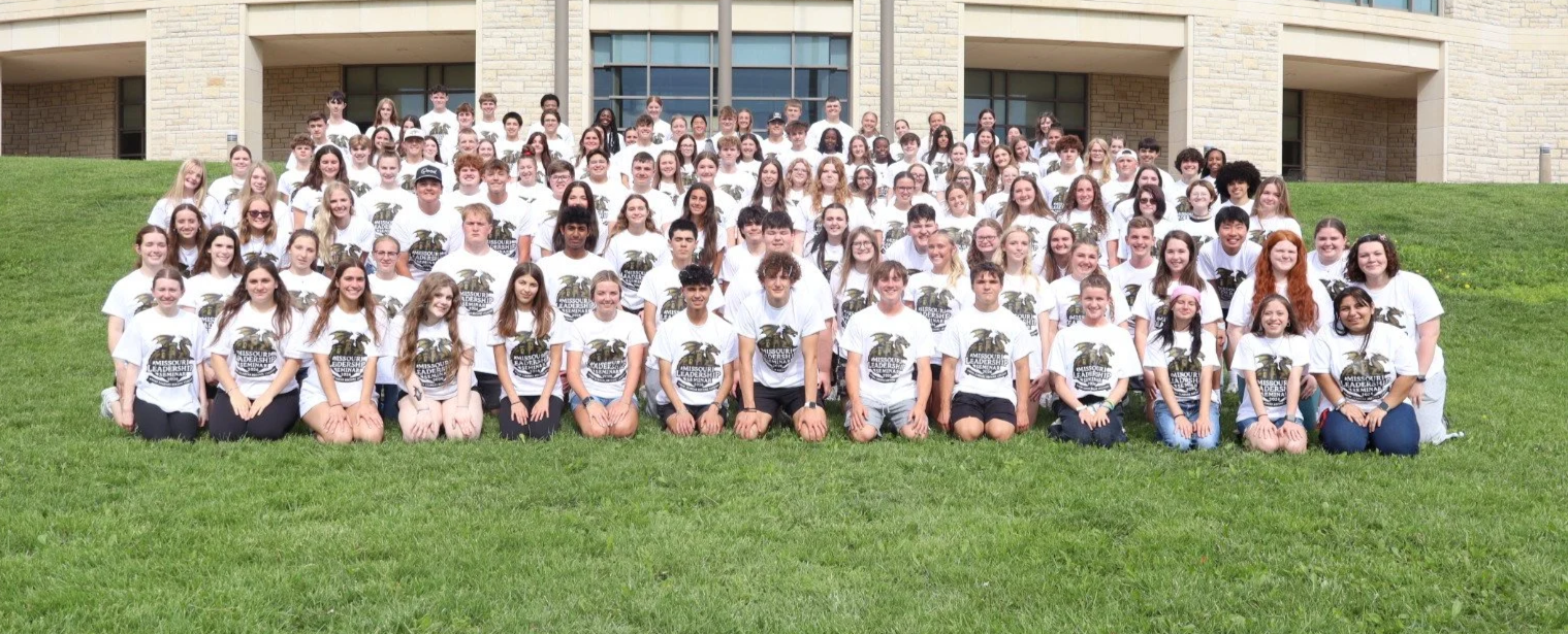 Large group of students in matching Missouri Leadership Seminar T-shirts posing on a lawn outside a school building.
