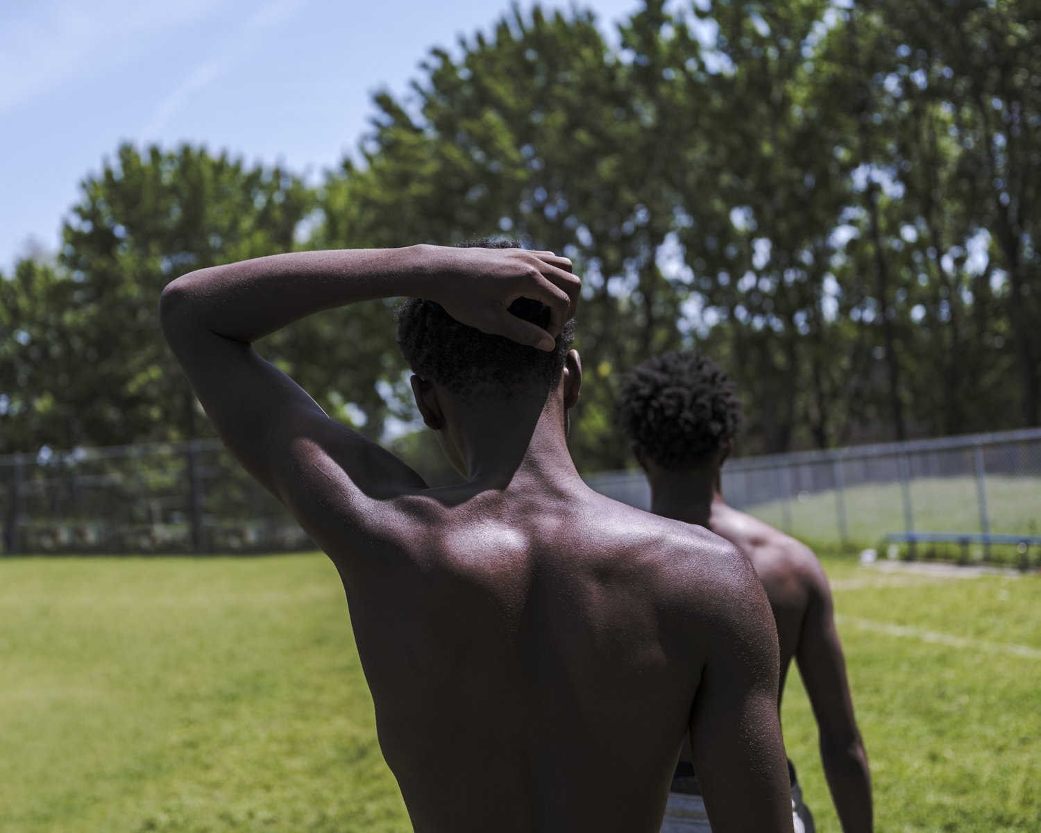Two Black men without shirts on in Oscar Peterson Park, Montreal.