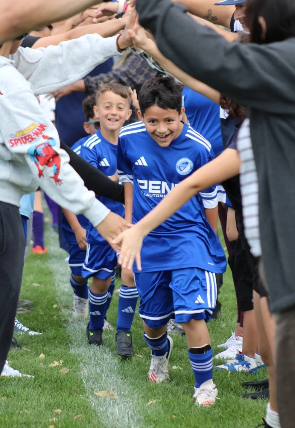 Young soccer players in blue jerseys forming a tunnel with their hands for a teammate to run through, all smiling.