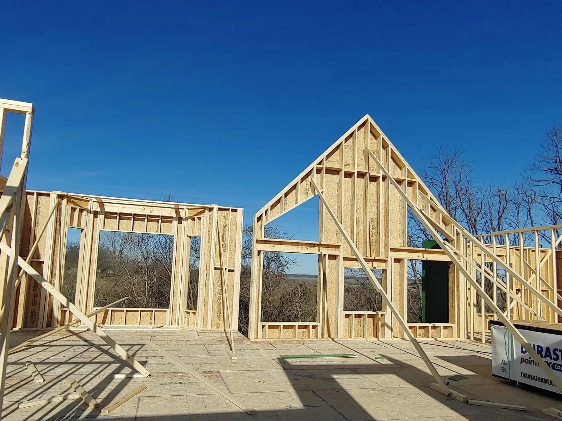 Wooden framing for a house under construction with clear blue sky and leafless trees in the background.