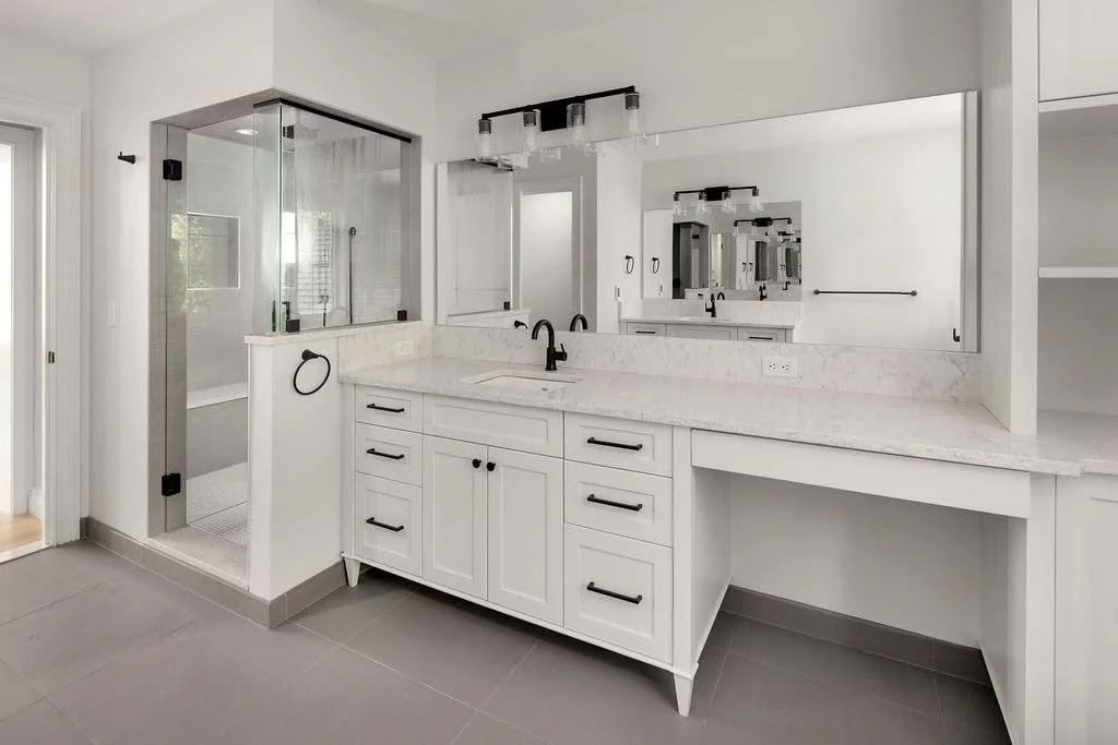 Modern bathroom with white cabinetry, large mirror, marble countertop, black fixtures, and a glass-enclosed shower.